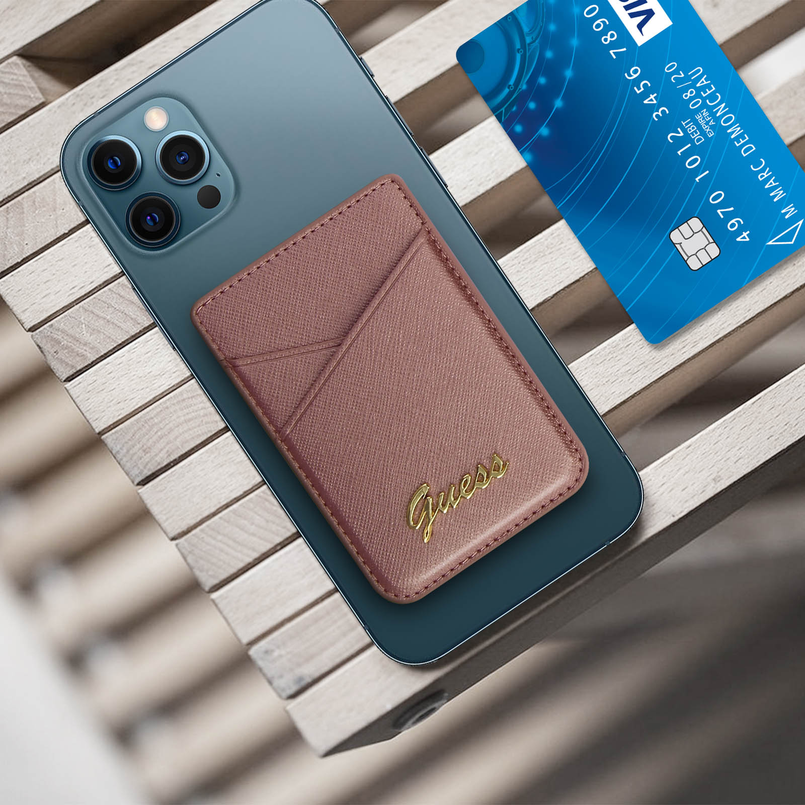 Braunes Telefon mit Guess-Geldbörse und Kreditkarte auf Holzoberfläche.
