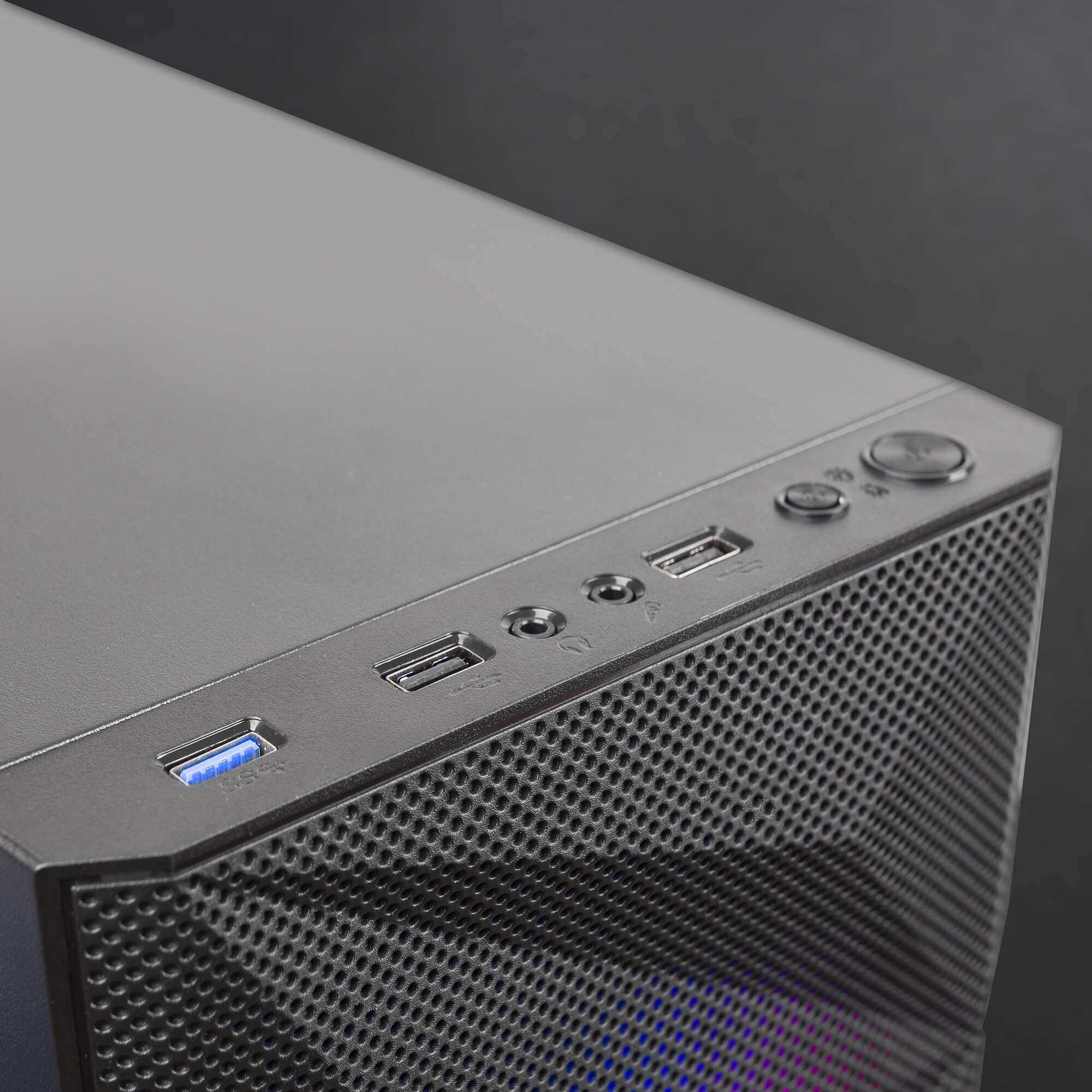 Zbliżenie na górną część obudowy komputera. Posiada porty USB, gniazdo audio, przyciski zasilania i resetowania oraz siatkę.