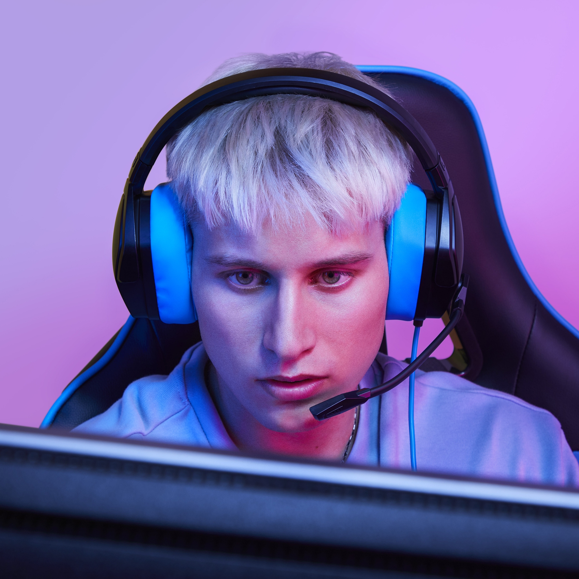 Una persona con cabello blanco usando auriculares azules, mirando un monitor.