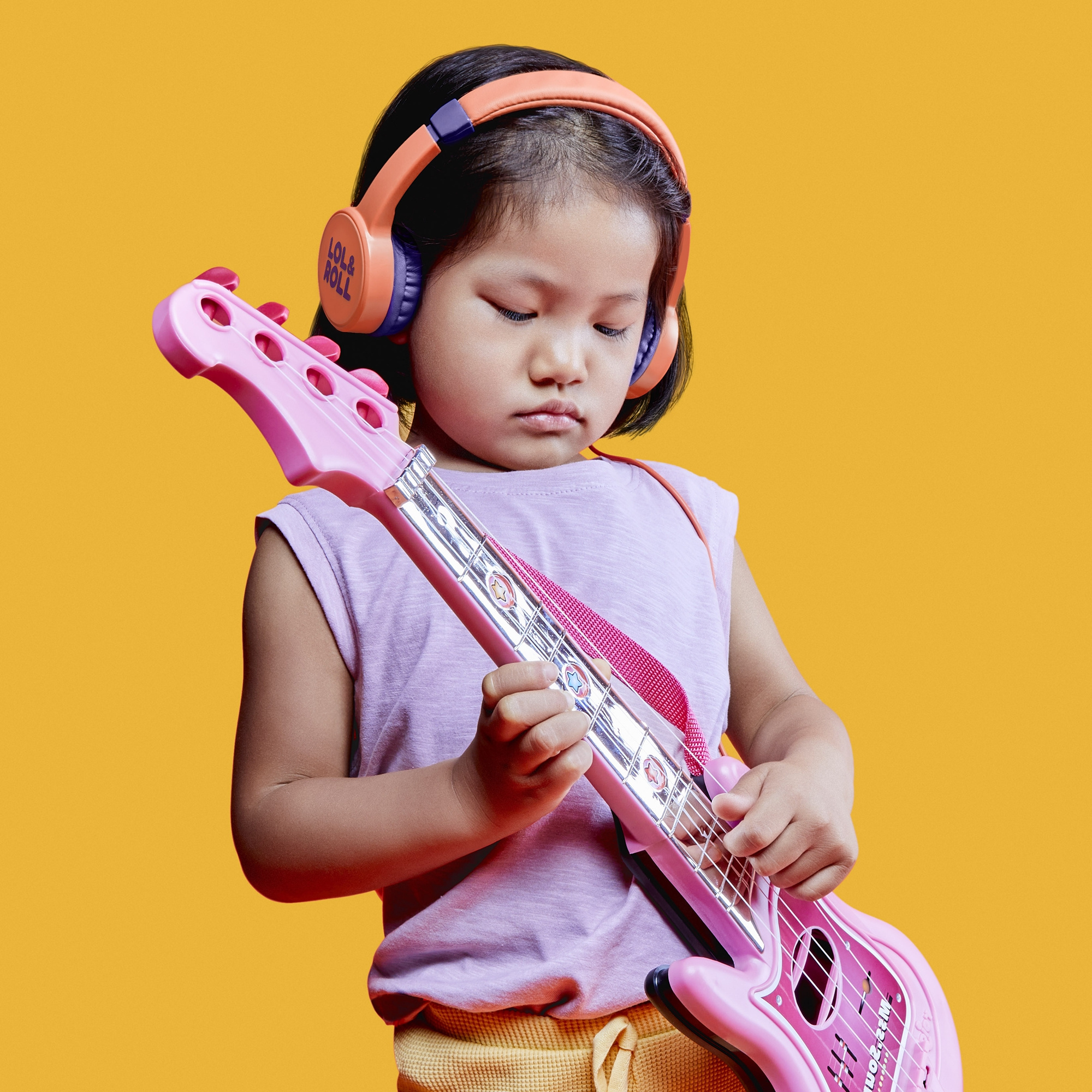 Niña tocando una guitarra de juguete rosa. Fondo naranja con auriculares coloridos.