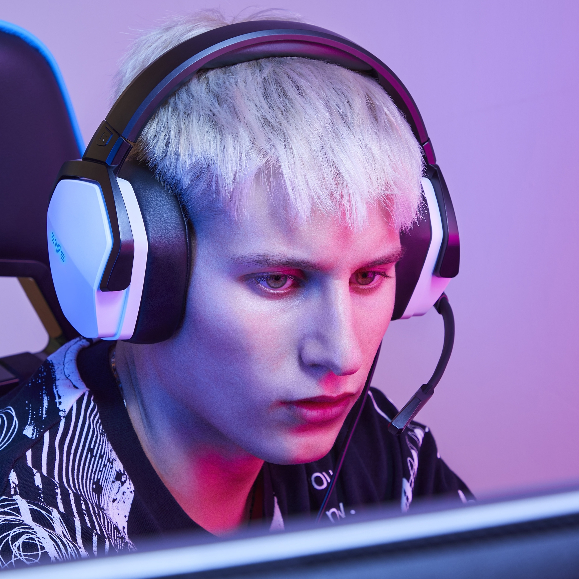 Un joven con auriculares y micrófono, en una habitación con iluminación rosa y azul.