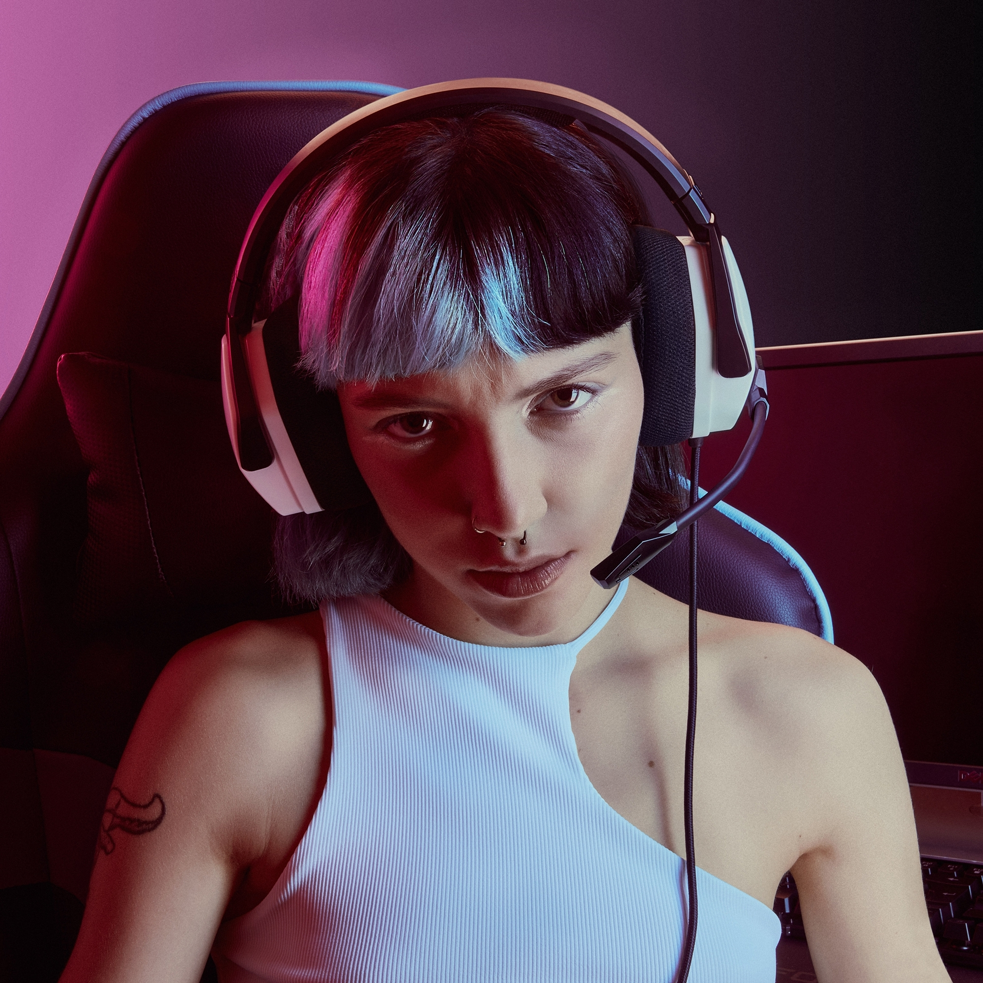 Mujer con auriculares mirando a la cámara. Fondo rosa y negro, expresión seria.
