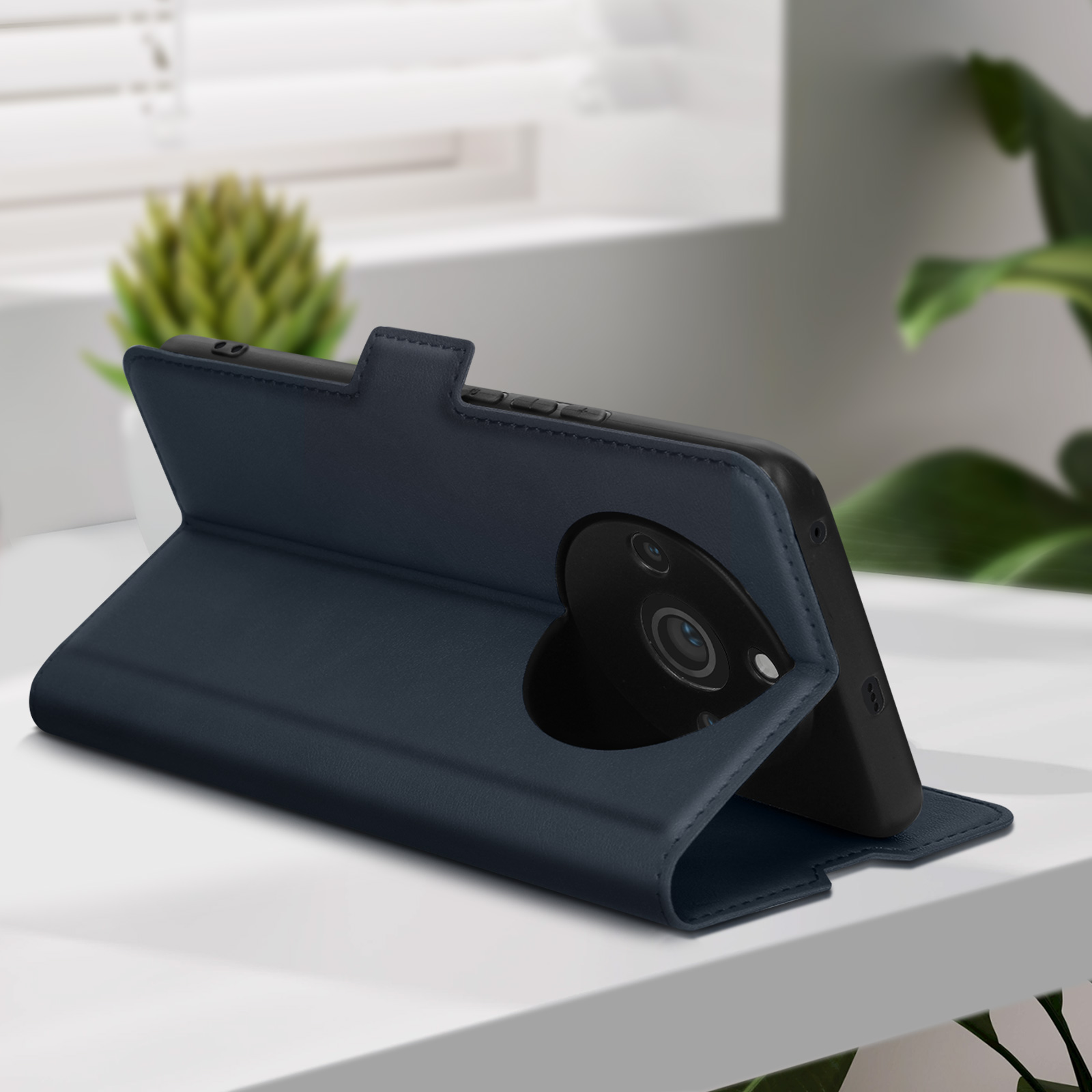 Marineblaue Handyhülle mit Telefon. Hülle ist offen, Telefon sichtbar. Weißer Tisch und grüner Pflanzenhintergrund.