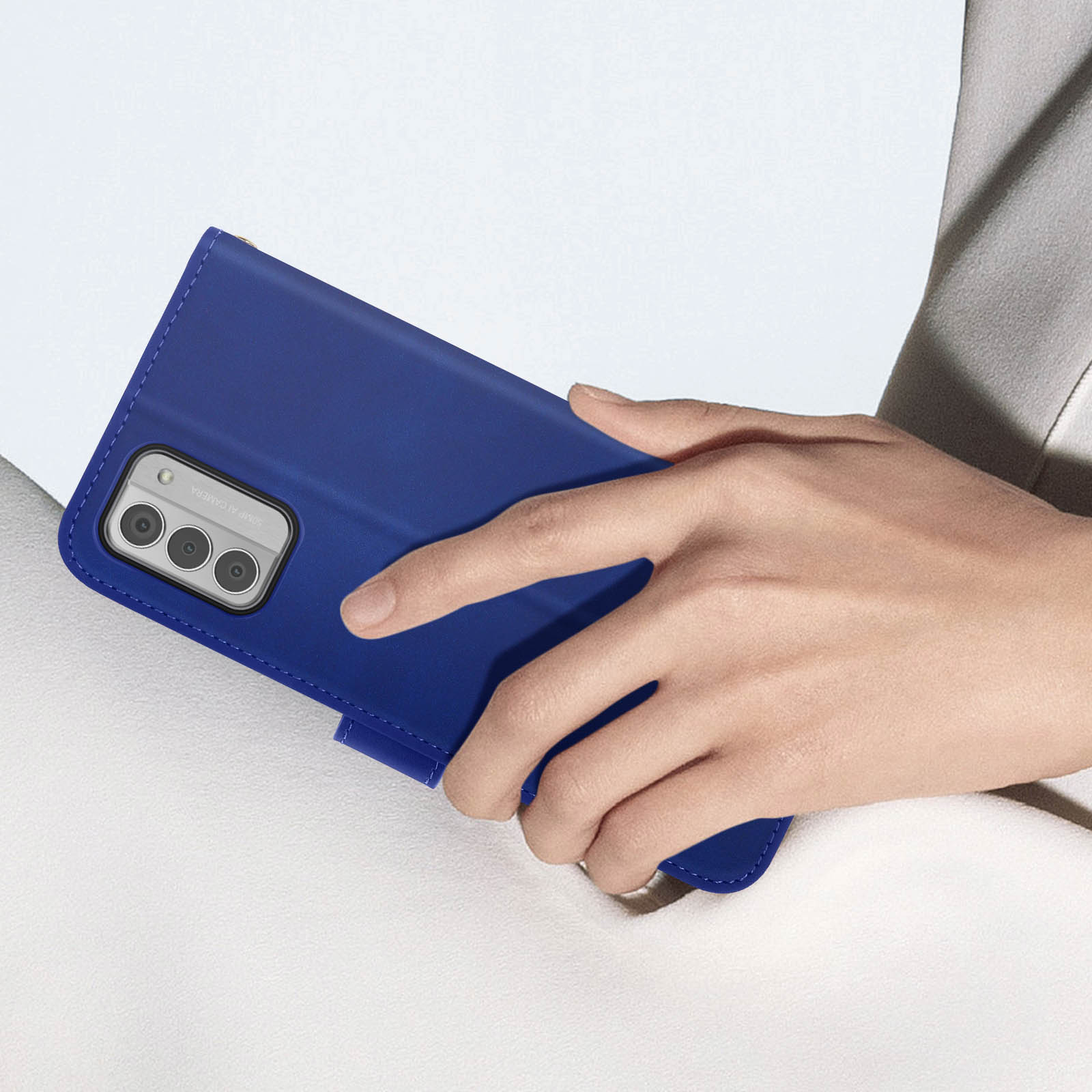 Una mano che tiene una custodia blu per telefono, sopra una superficie bianca. La custodia ha tre fotocamere.