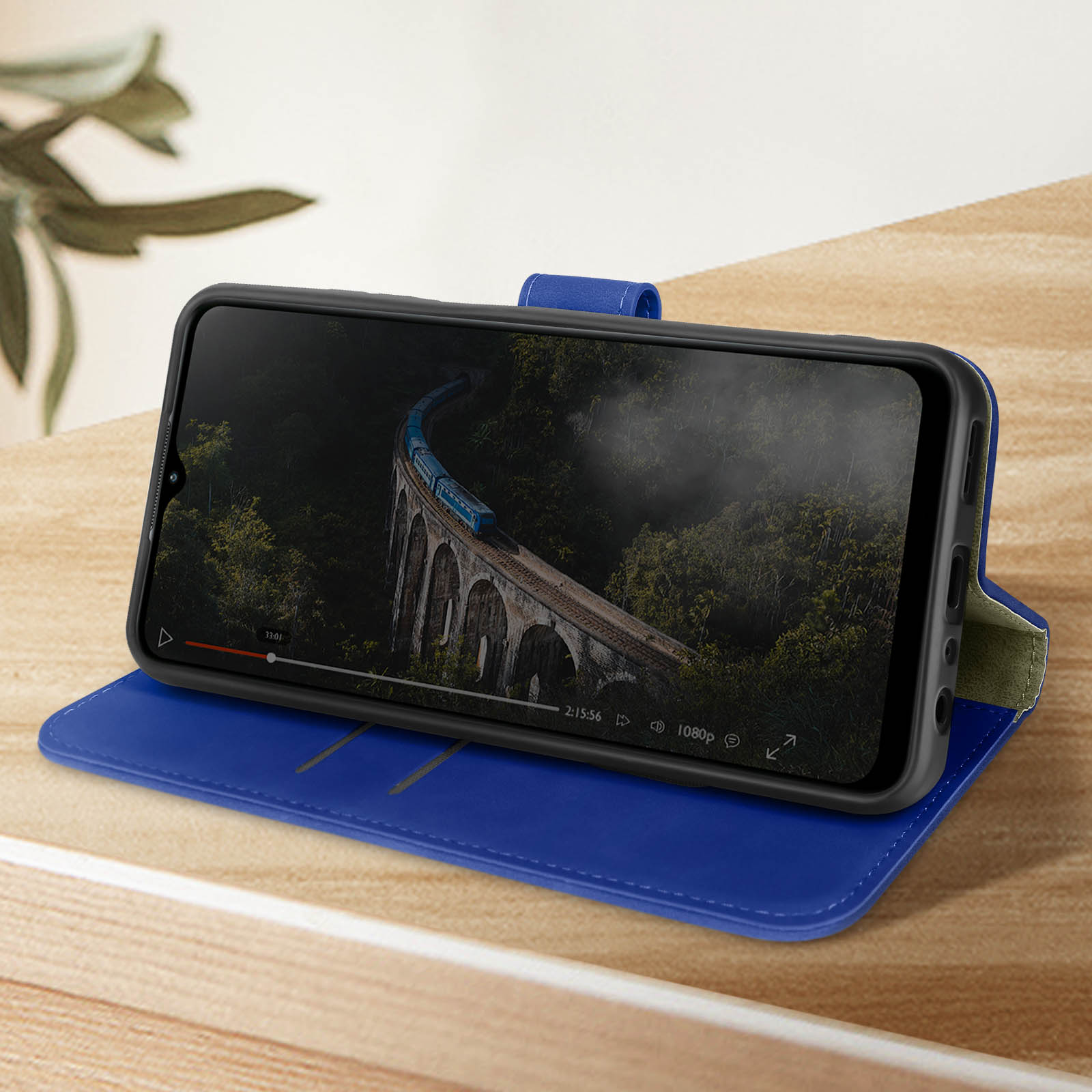 Un telefono in una custodia blu mostra un video di un treno su un ponte. La custodia è aperta su un tavolo di legno.