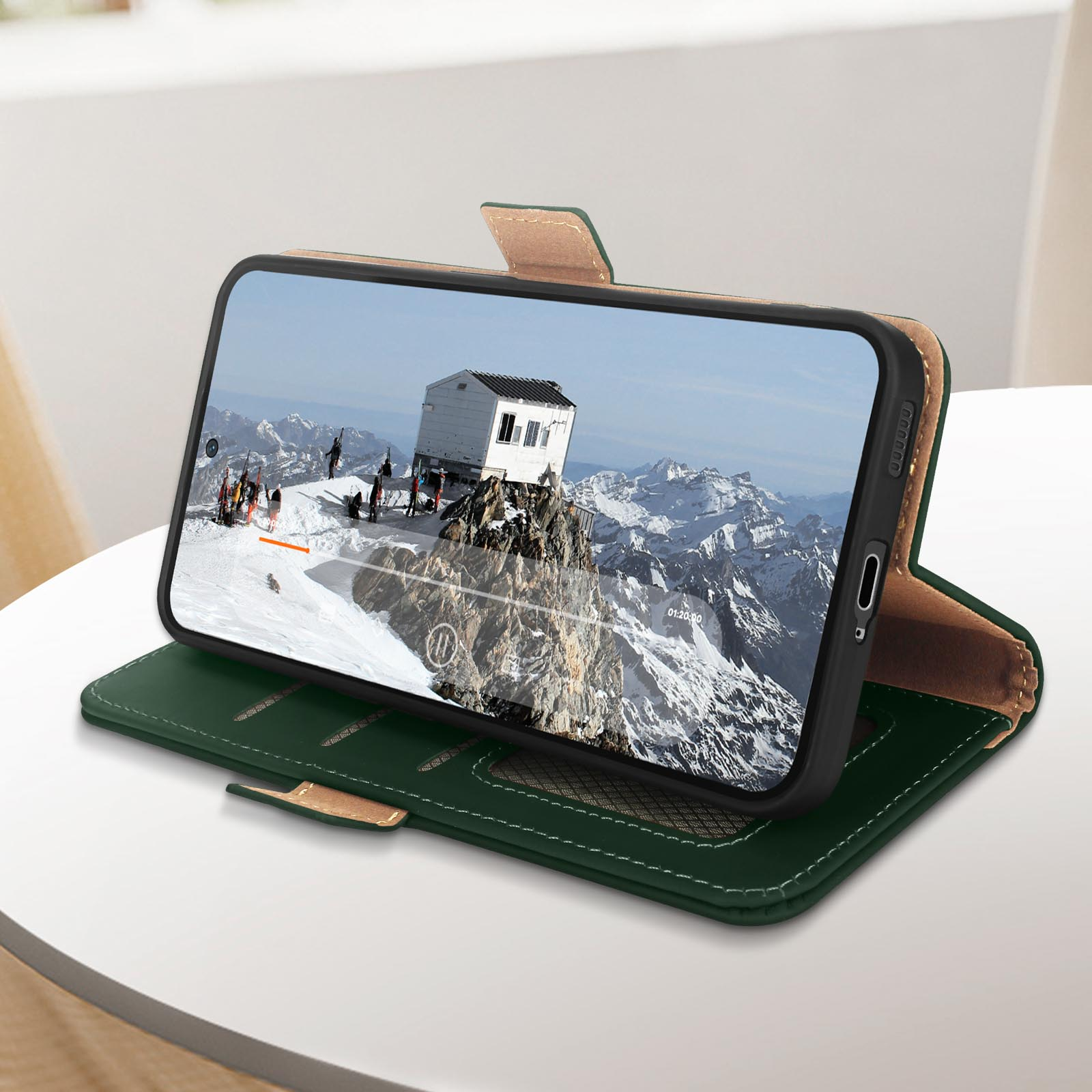 Custodia per telefono con scena di montagna sullo schermo, aperta su un tavolo, con custodia verde e beige.
