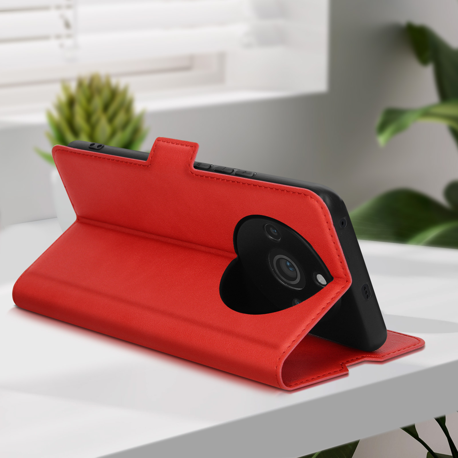 Una custodia per telefono rossa aperta su un tavolo, telefono dentro, con una pianta verde sullo sfondo.