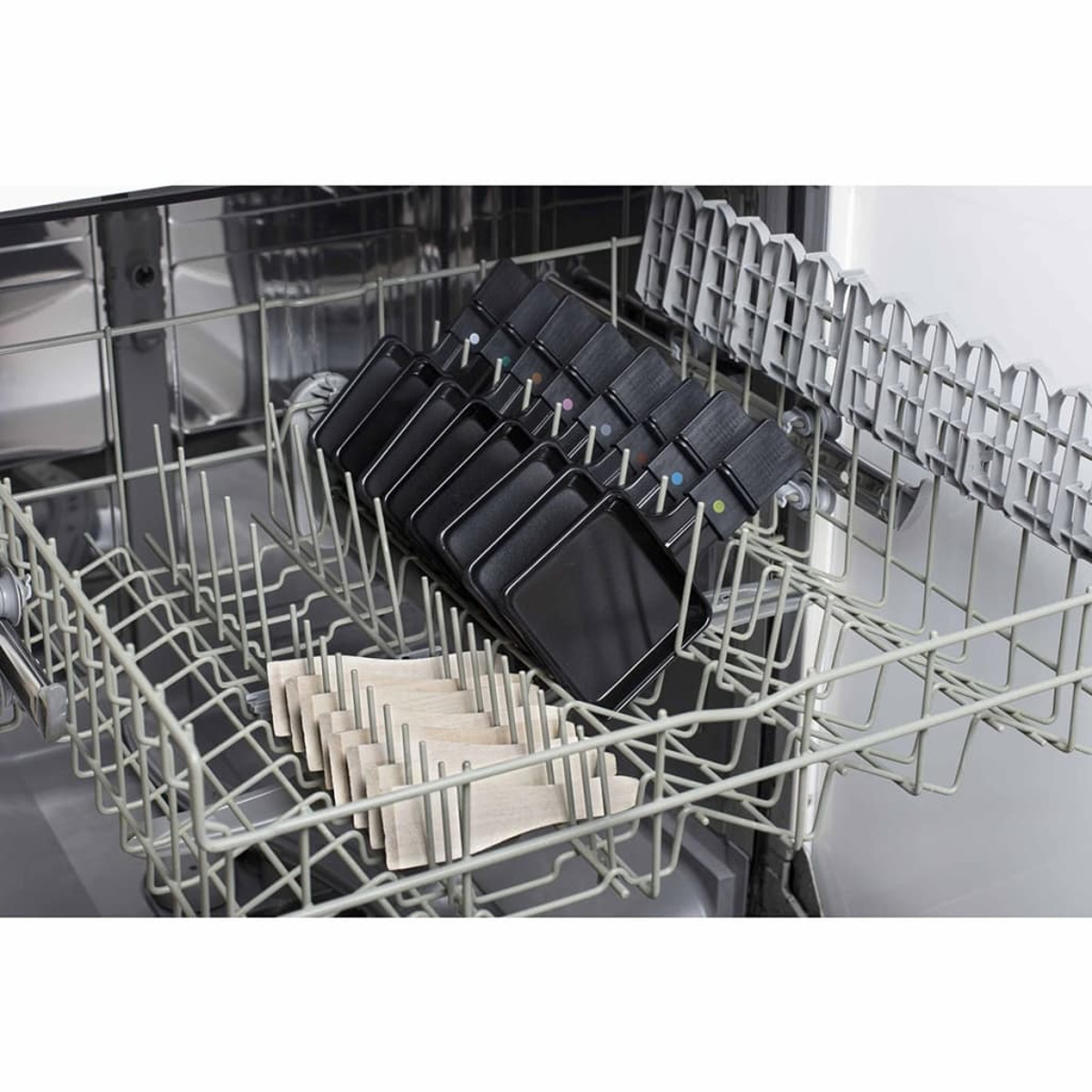 Wnętrze zmywarki z przedmiotami w koszach. W koszach znajdują się czarne kwadraty i beżowe prostokąty.