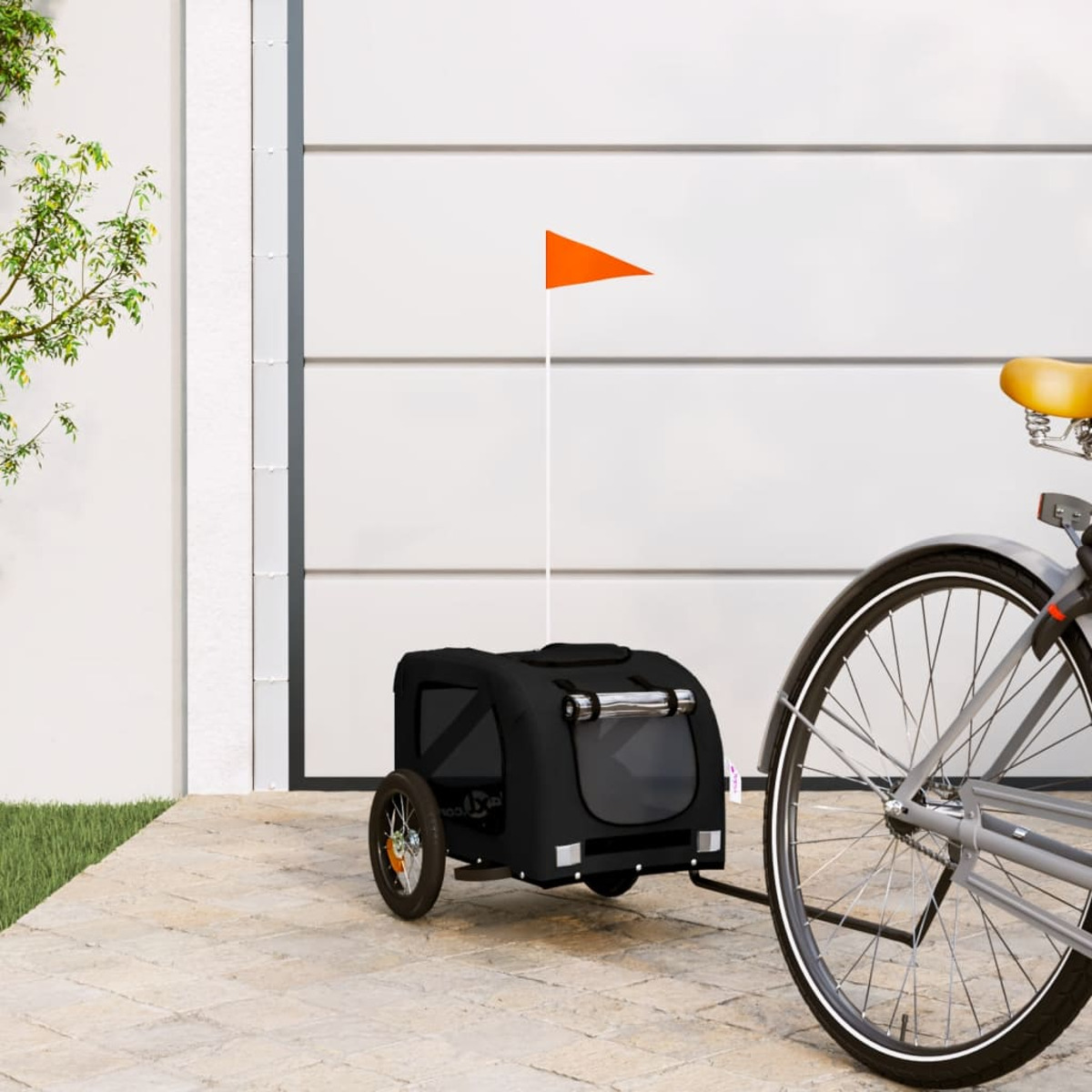 Ein schwarzer Tieranhänger an einem Fahrrad, mit einer orangefarbenen Flagge. Der Hintergrund ist ein weißes Garagentor.