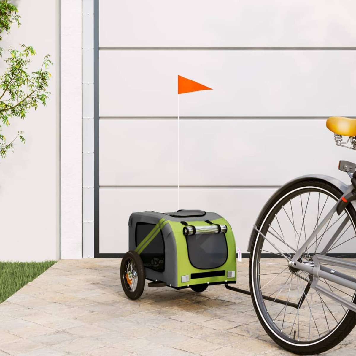 Fahrradanhänger mit orangefarbener Flagge, die an einem Fahrrad auf einer gepflasterten Oberfläche befestigt ist.