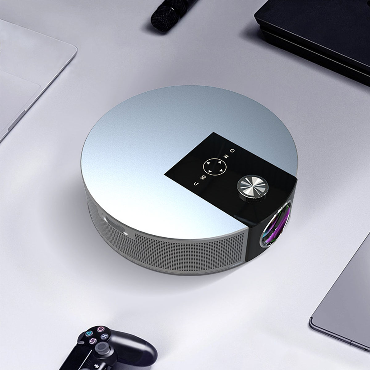 Silberner Projektor mit schwarzem Bedienfeld, in der Nähe von Laptop, Gamecontroller usw.