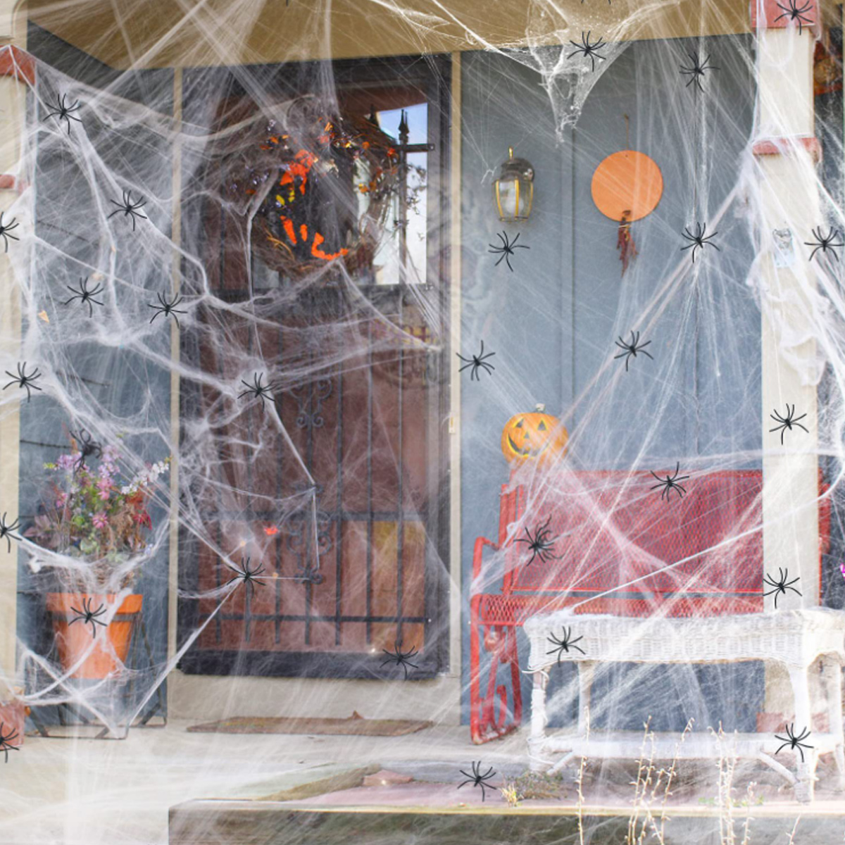 Eine Halloween-dekorierte Veranda mit Spinnweben, Spinnen, einem Kürbis und einer Bank. Die Tür hat ein dunkles Eisentor.