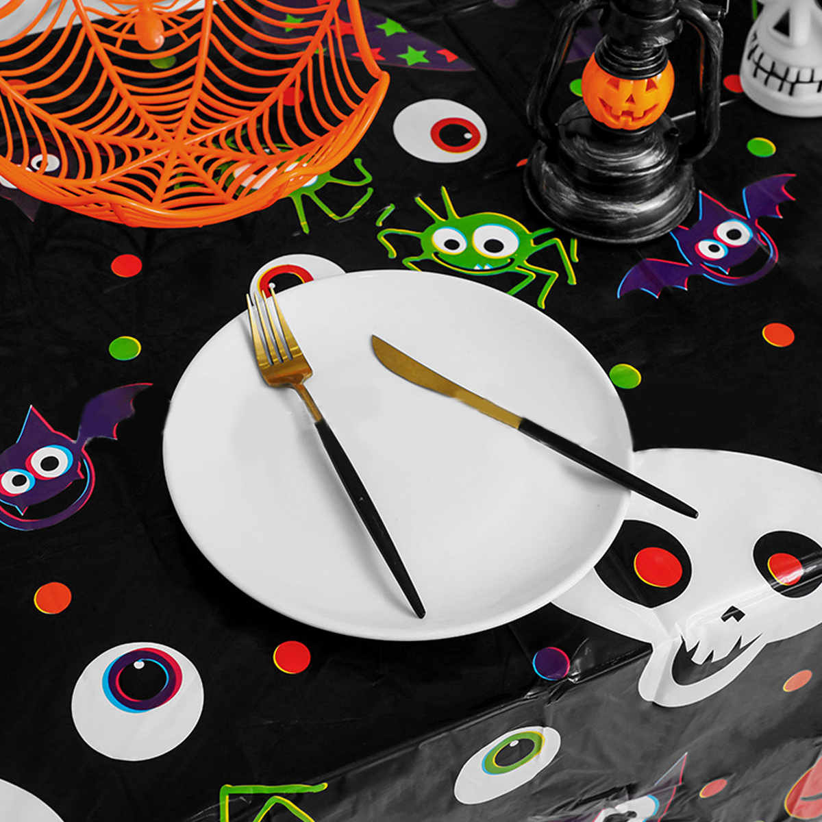 Halloween-Tischdekoration mit Teller, Gabel und Messer, umgeben von Dekorationen wie Fledermäusen und einem Spinnennetz.