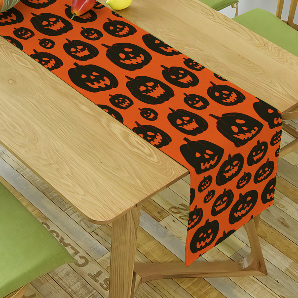 Oranger Halloween-Tischläufer mit schwarzen Kürbisformen auf Holztisch.