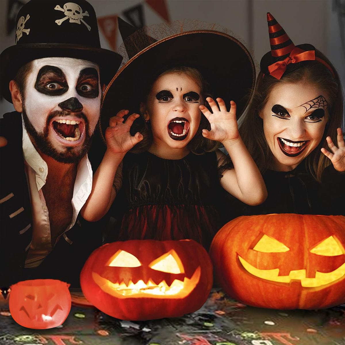 Familie in Halloween-Kostümen mit geschnitzten Kürbissen und einem kleinen Kürbis im Vordergrund.