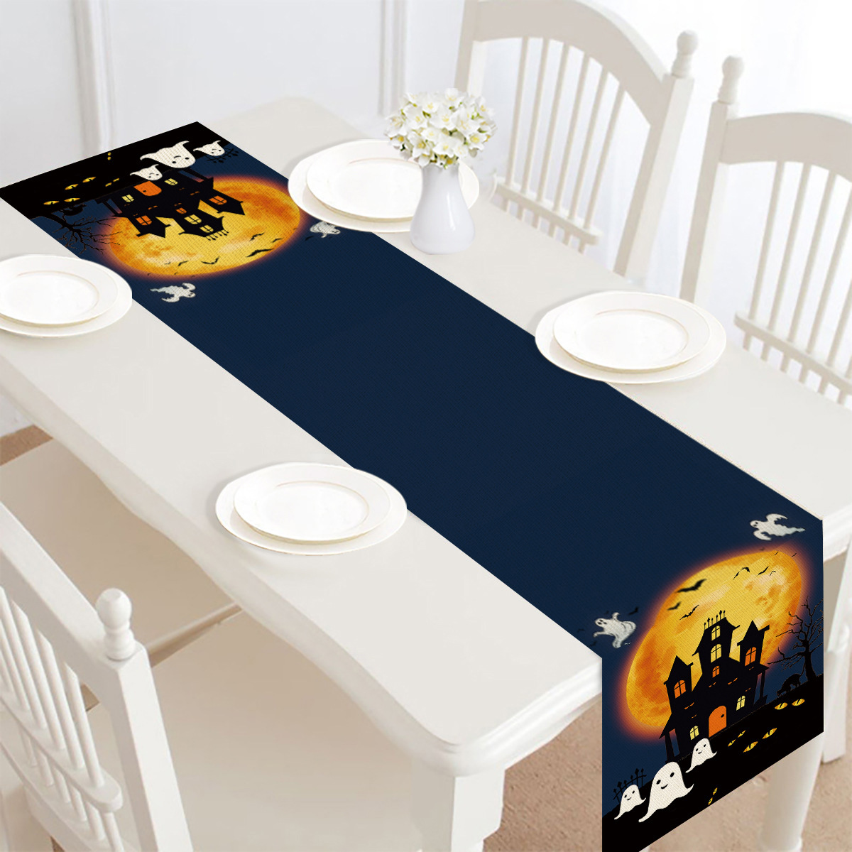 Halloween-Tischläufer mit Spukschloss, Vollmond und Geistern auf einem weißen Tisch mit Stühlen.