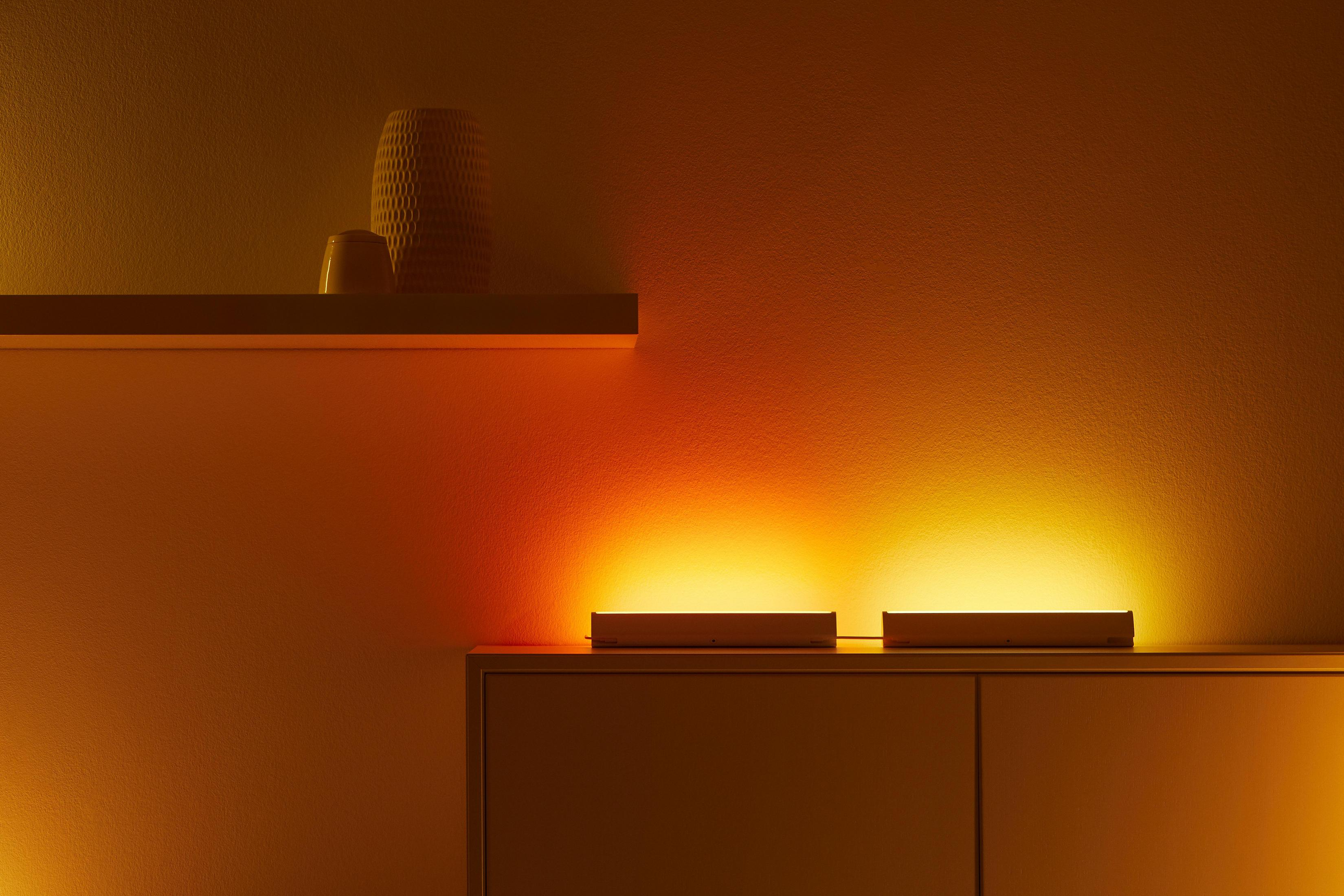 Warmtoniger Raum mit zwei linearen Lichtern und einer dekorativen Vase auf einem Regal. Beige Wand.