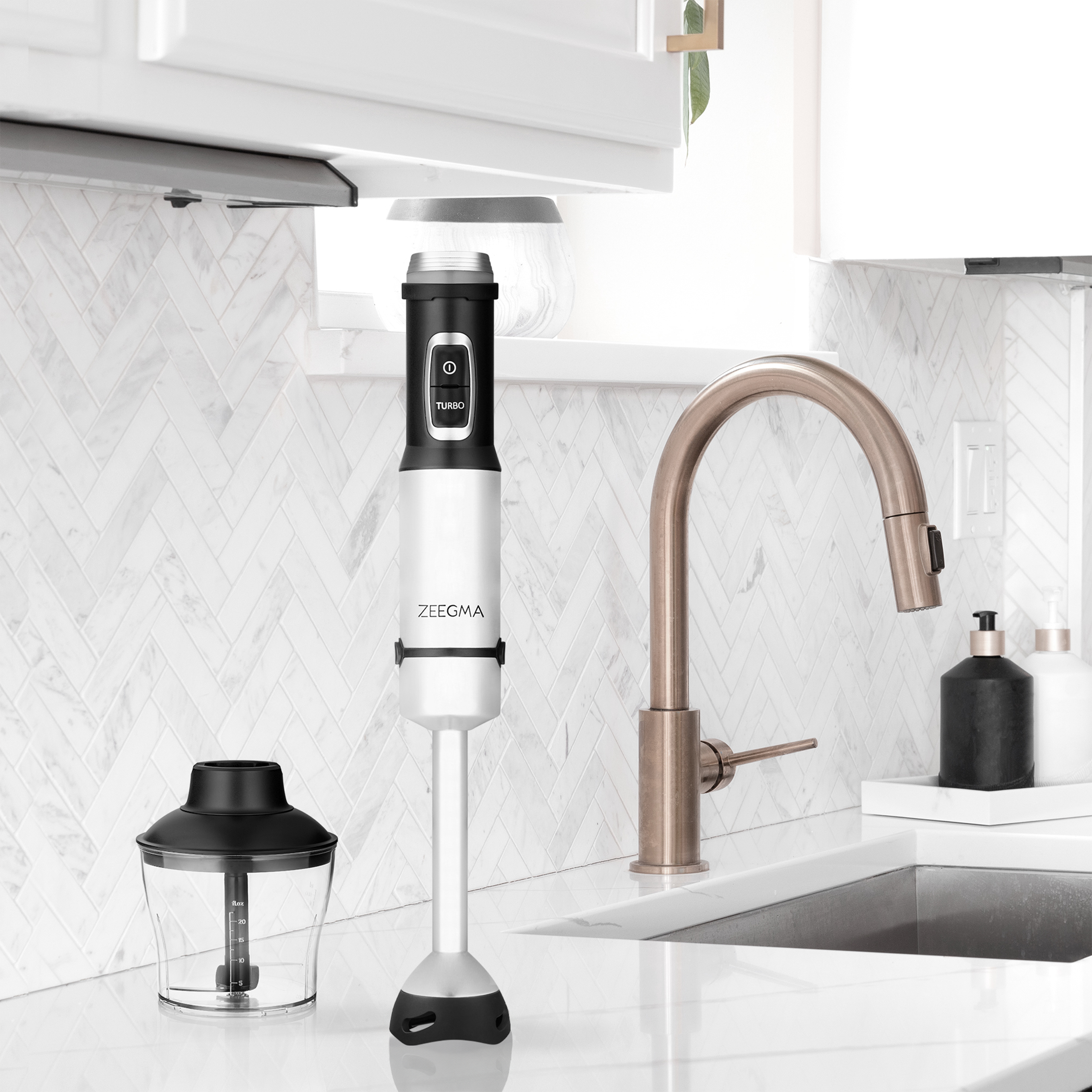 Biało-czarny blender zanurzeniowy obok pojemnika i kranu w otoczeniu kuchni.