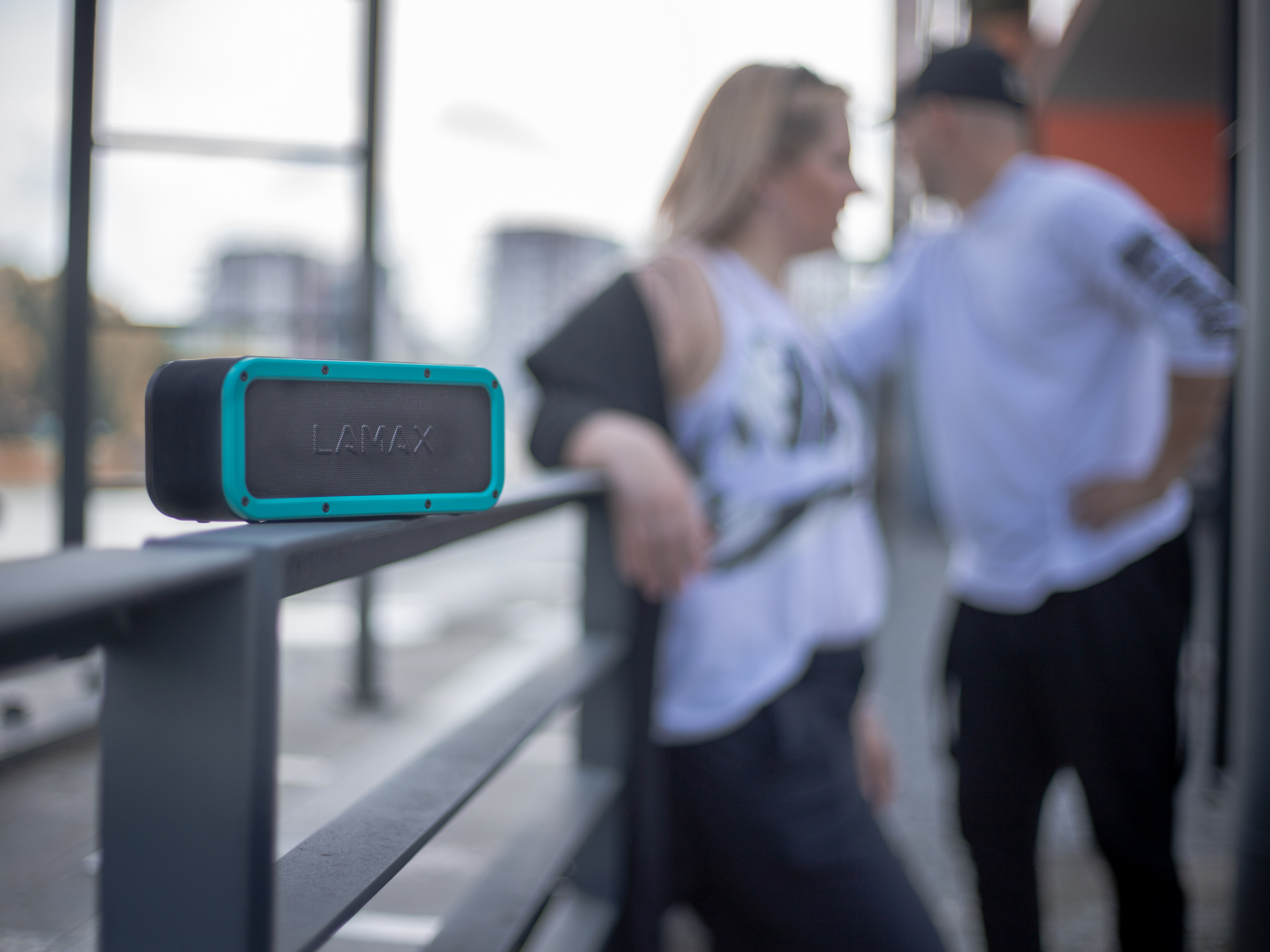 Turkusowy i czarny głośnik Bluetooth. Para stoi obok z rozmytym tłem.