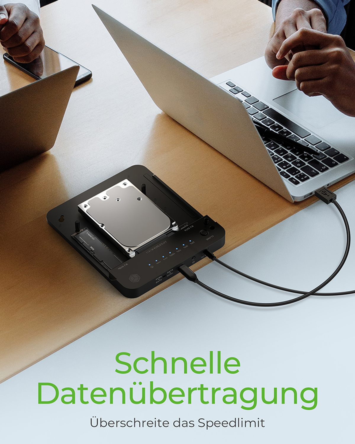 Zwei Personen arbeiten mit Laptops, und ein Gerät mit interner Festplatte ist angeschlossen.