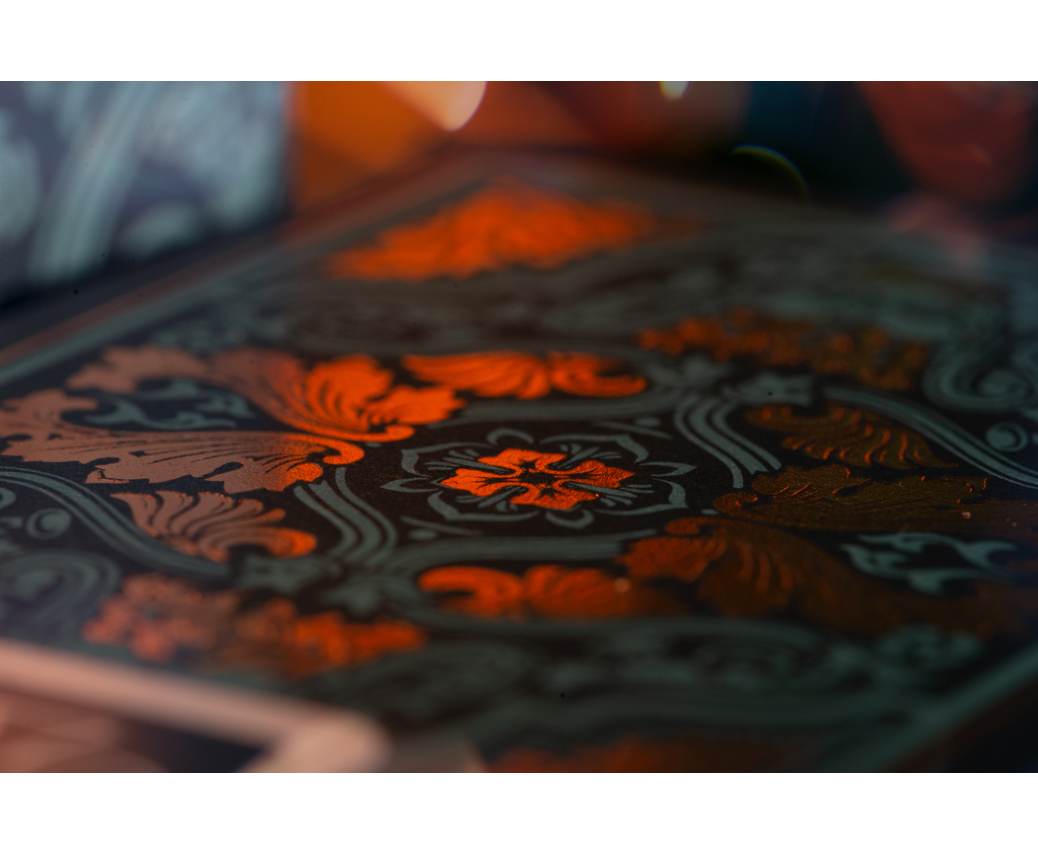 Nahaufnahme eines verzierten Buchcovers mit floralem Muster. Es ist dunkel mit orangefarbenen Details.