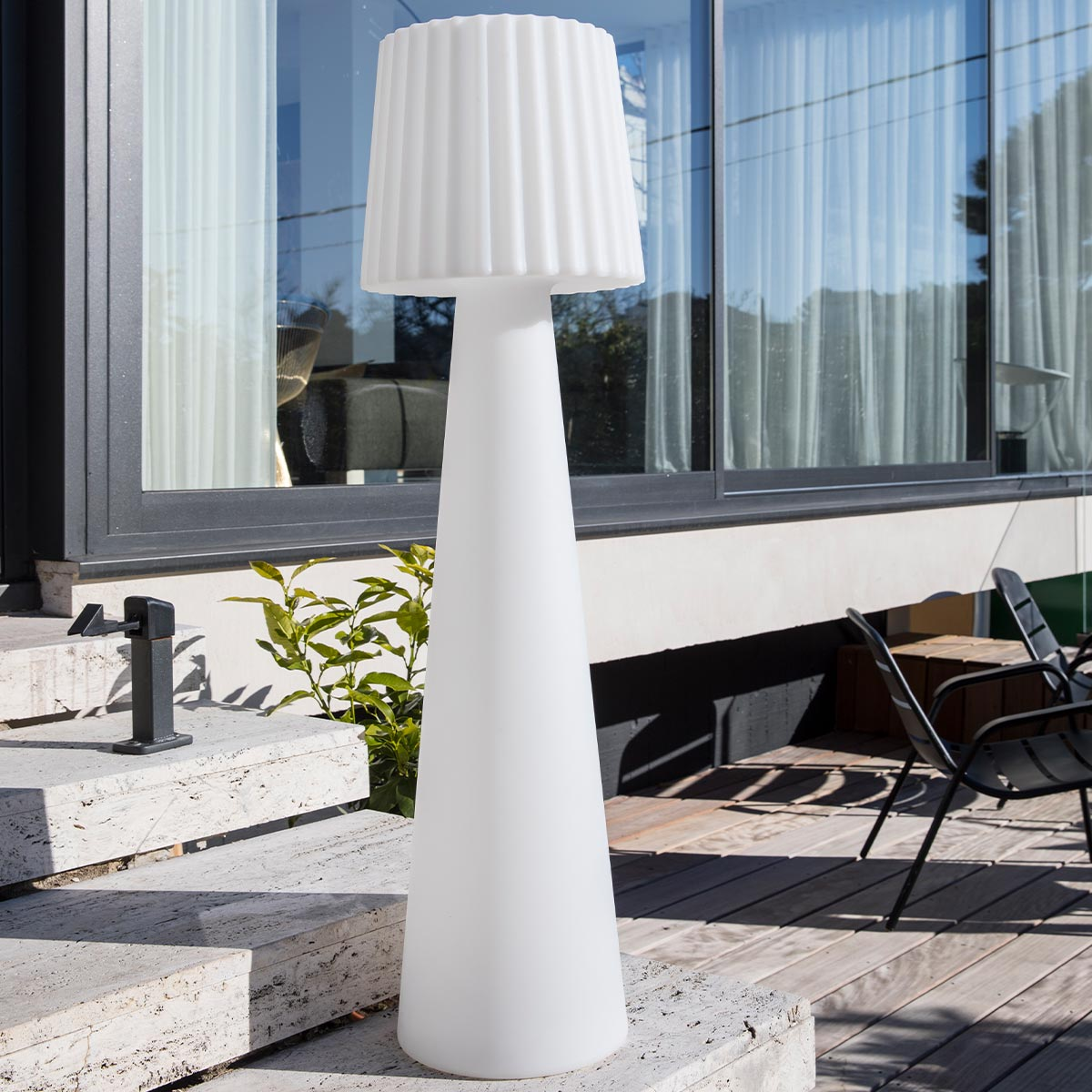 Una lampada da esterno bianca alta con paralume scanalato su un patio con gradini e un giardino.