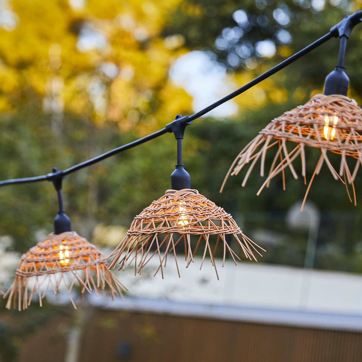 Lichterkette mit drei gewebten Lampenschirmen. Warmes Licht, hängend an einem schwarzen Draht. Gelber Hintergrund.