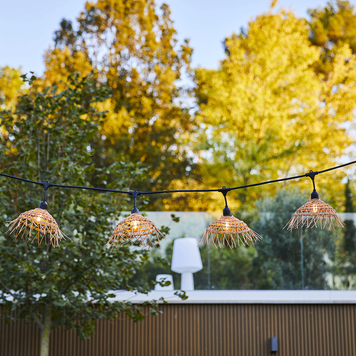 Lichterkette mit gewebten Lampenschirmen, die vor einem verschwommenen Gartenhintergrund hängen.