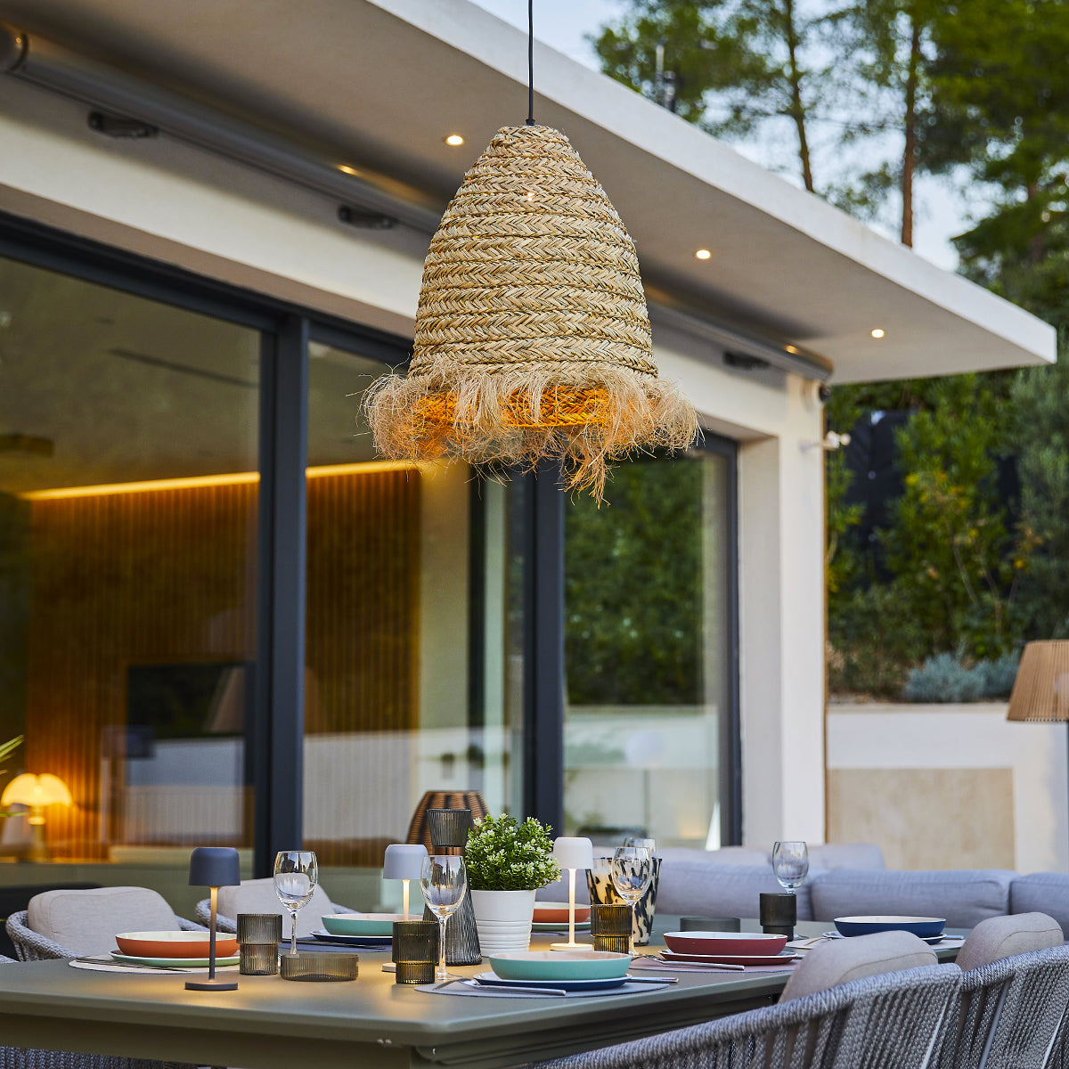 Essbereich im Freien mit einer gewebten Lampe über einem Tisch mit Essen und Gläsern.