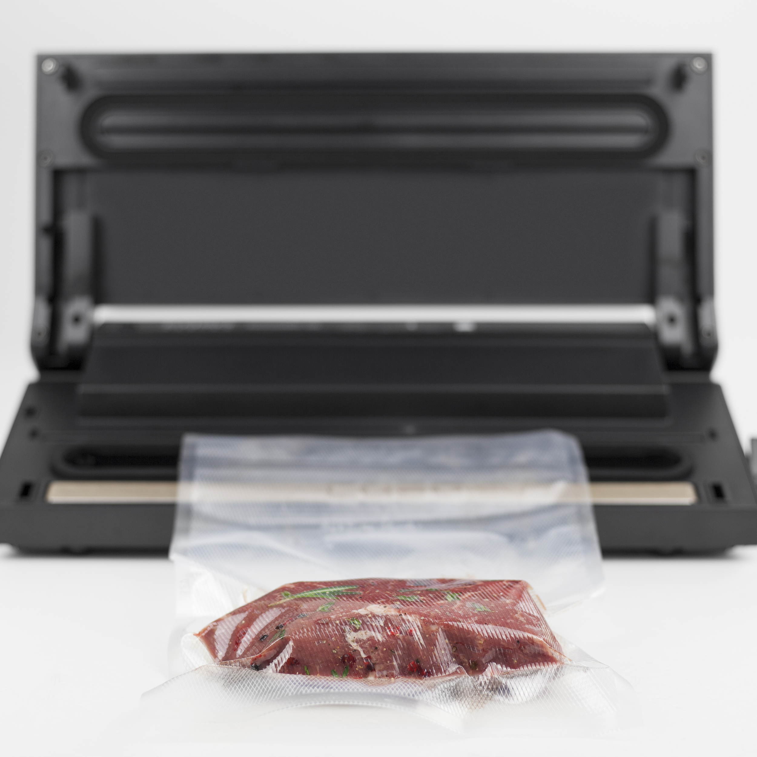 Ein Vakuumierer mit einem Steak in einer Tüte. Schwarze Maschine im Hintergrund und weiße Oberfläche.