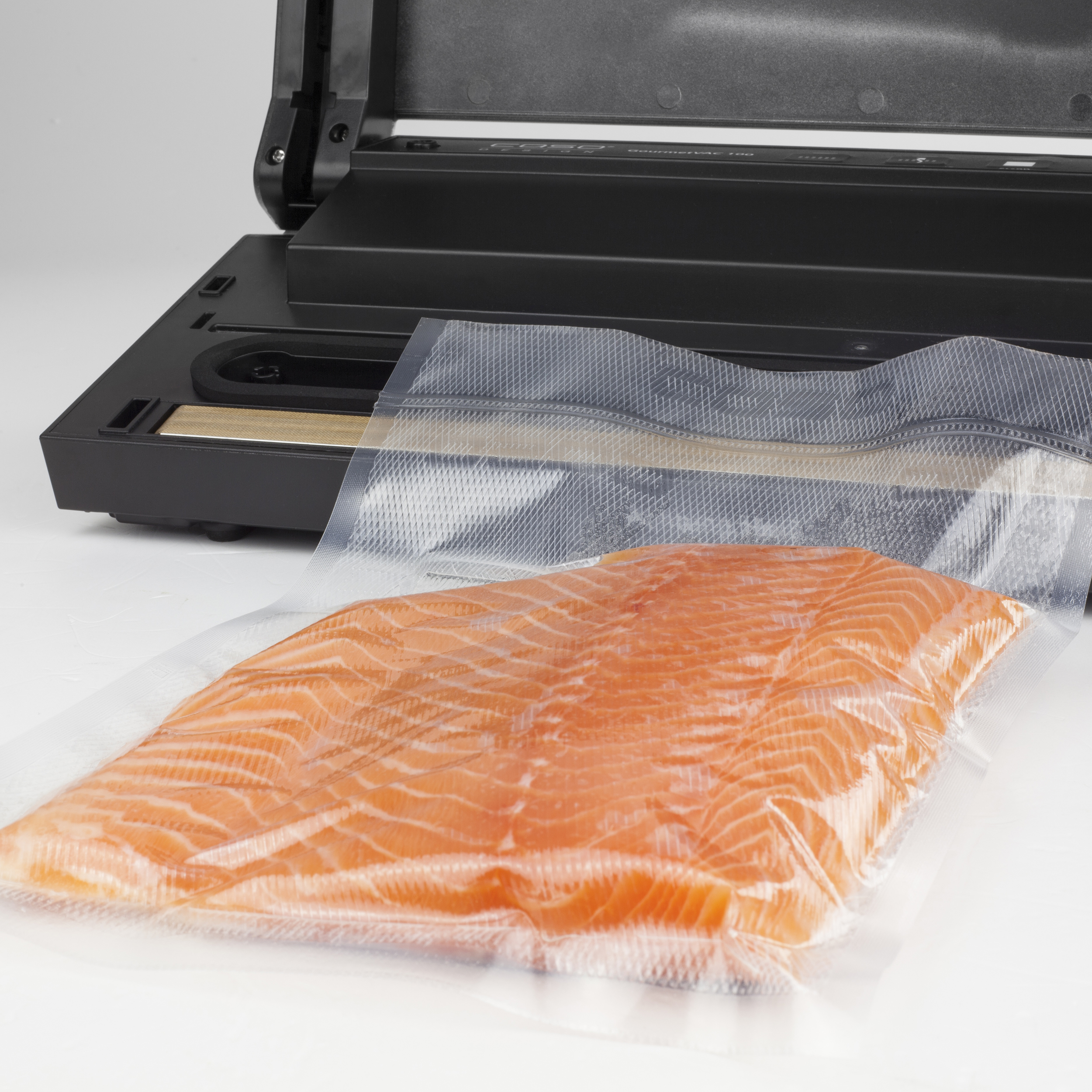 Vakuumierer mit Lachsfilet in einem durchsichtigen Beutel. Weißer Hintergrund. Schwarzes Gerät.