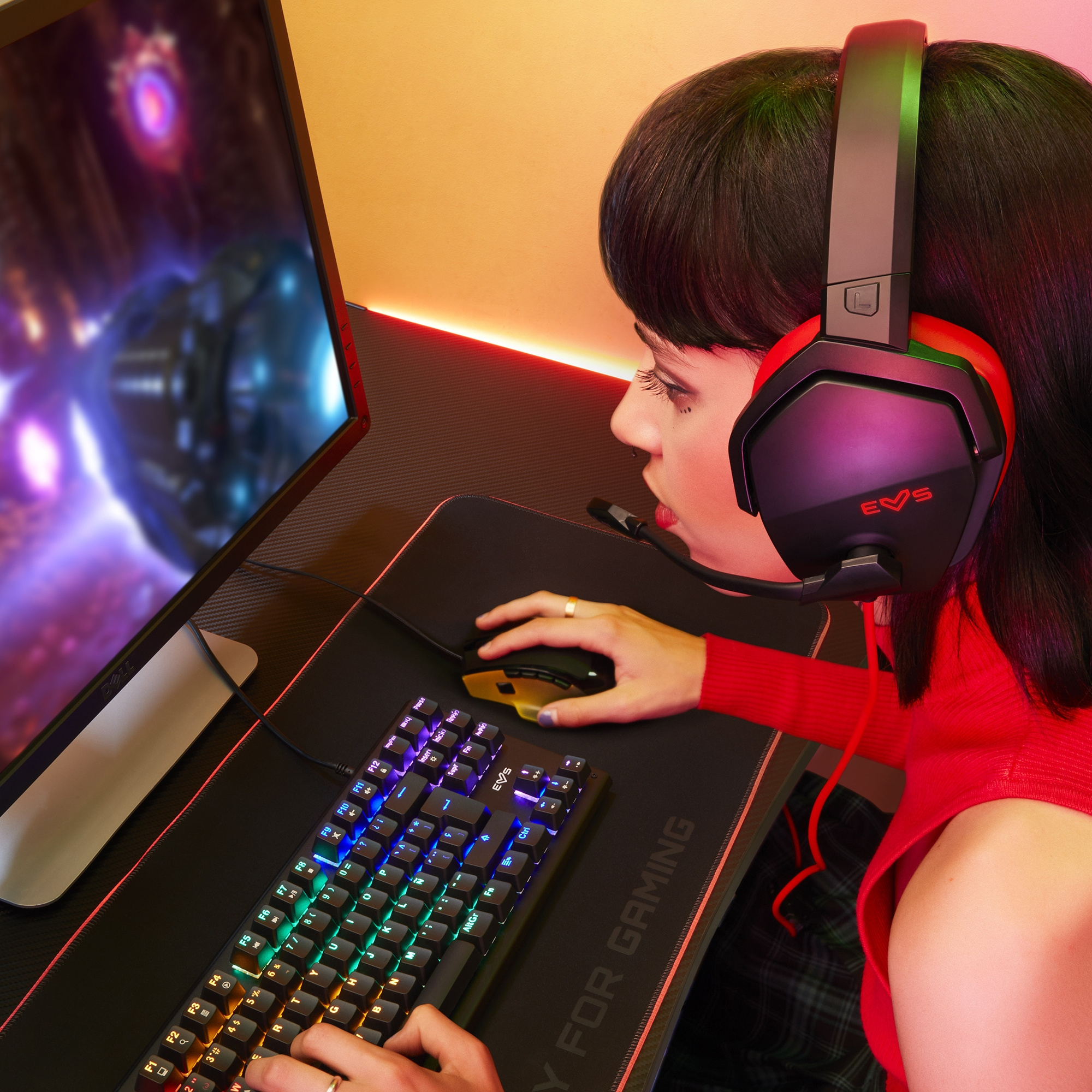 Kobieta grająca w gry z słuchawkami, klawiaturą i myszką. Widoczny monitor i podkładka.