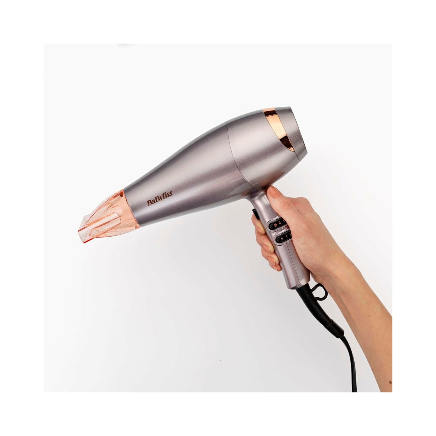 Ręka trzyma szarą suszarkę do włosów. Suszarka ma różowo-pomarańczową dyszę i czarny przewód.