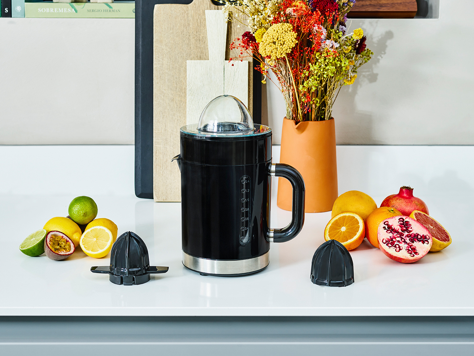 Czarna elektryczna wyciskarka do owoców z owocami. Zawiera pomarańcze, cytrynę, granat i limonkę.