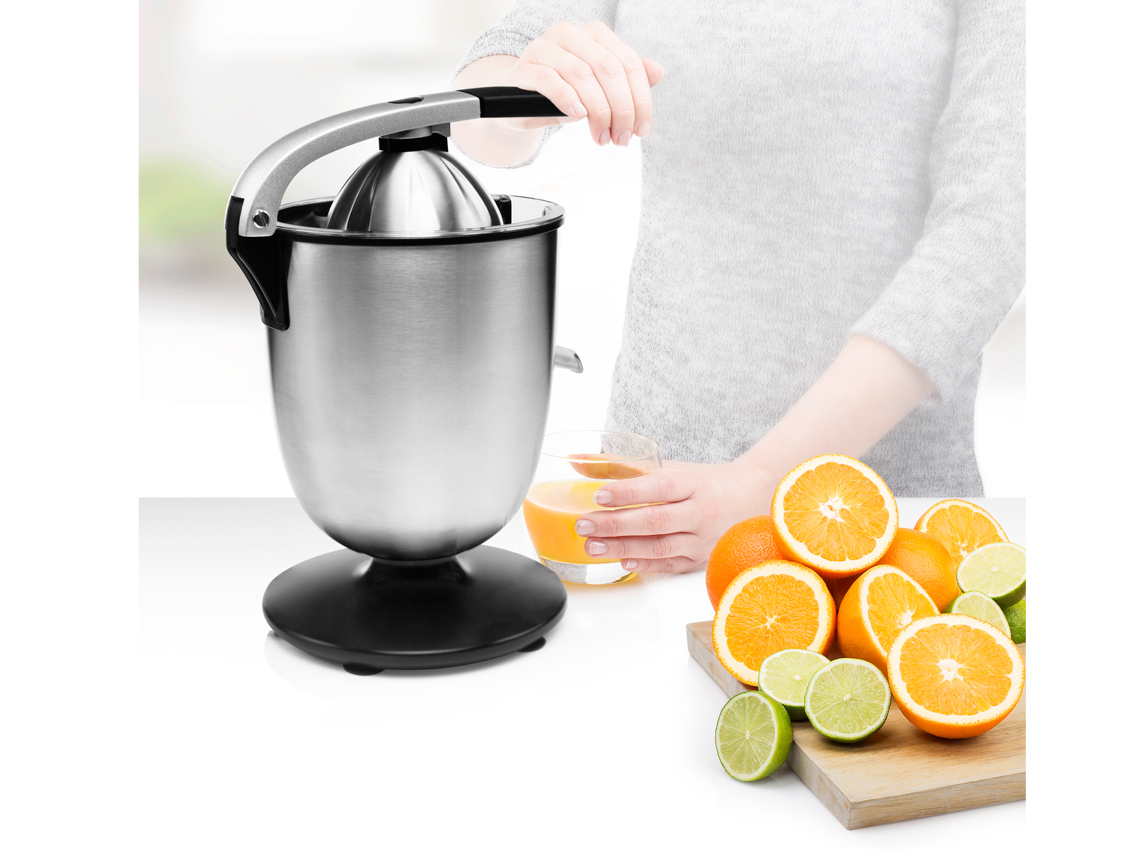 Osoba wyciskająca pomarańcze za pomocą wyciskarki ręcznej. Widoczne są pokrojone pomarańcze i limonki.