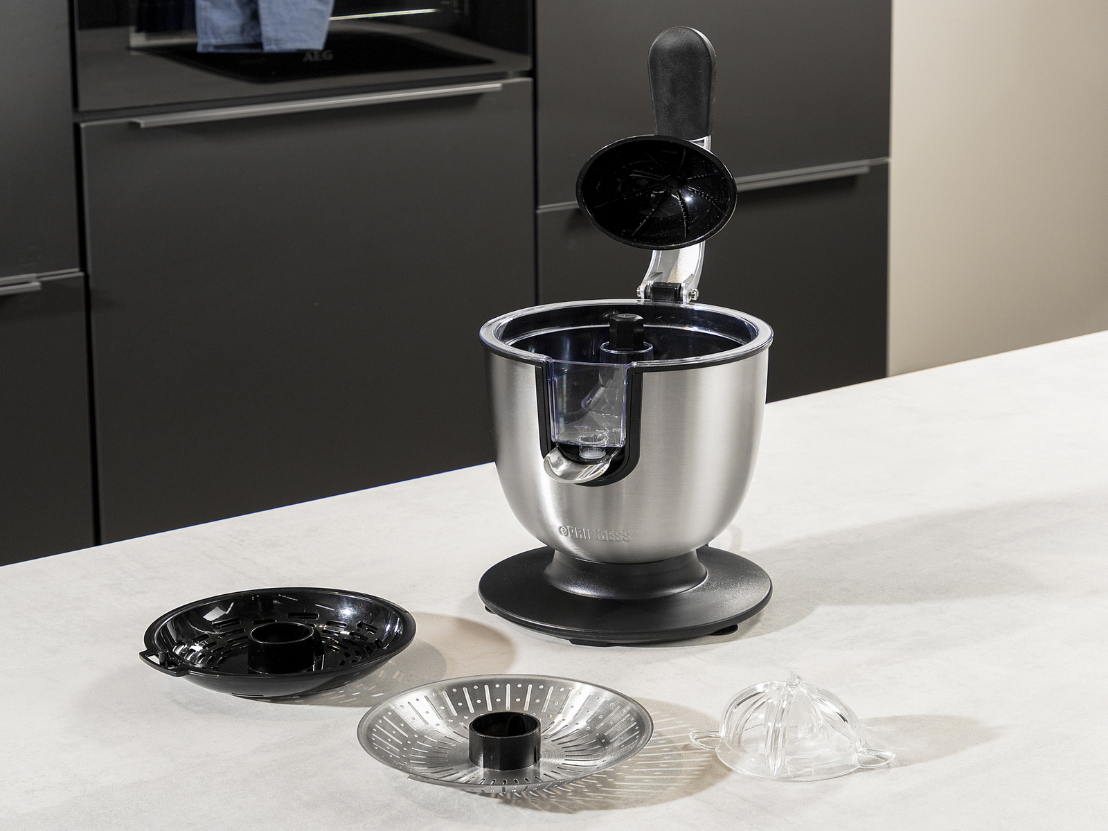 Urządzenie kuchenne ze stali nierdzewnej z odłączanymi częściami. Czarno-białe tło. Części: miska, sitko i wyciskarka do cytrusów.