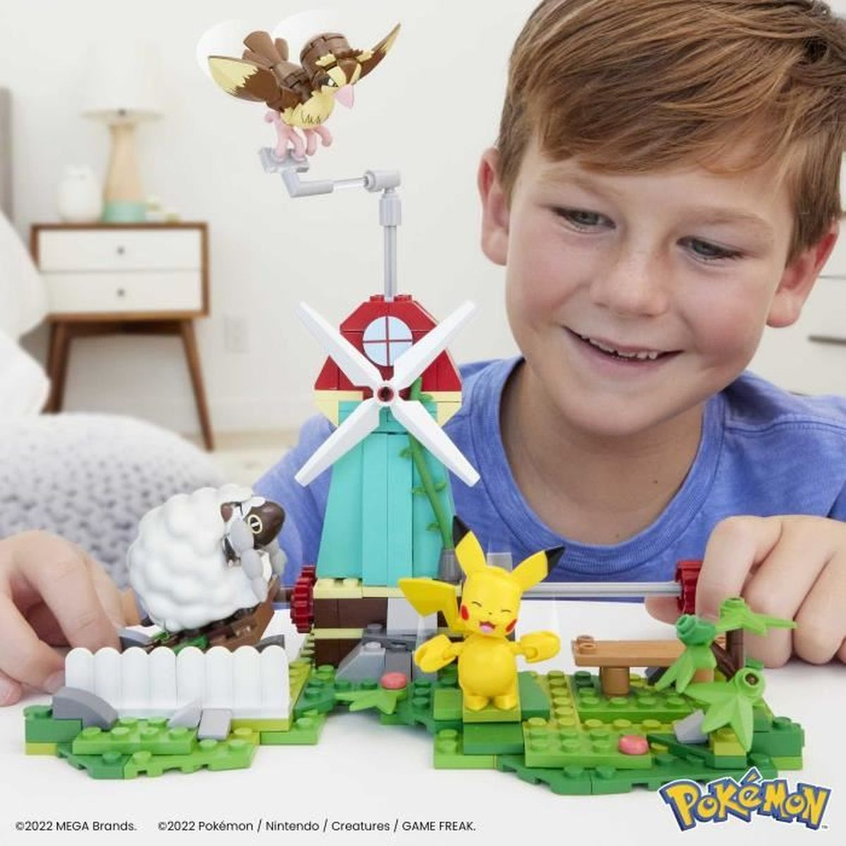 Chłopiec bawi się zestawem klocków Pokémon z Pikachu, wiatrakiem i innymi figurami.