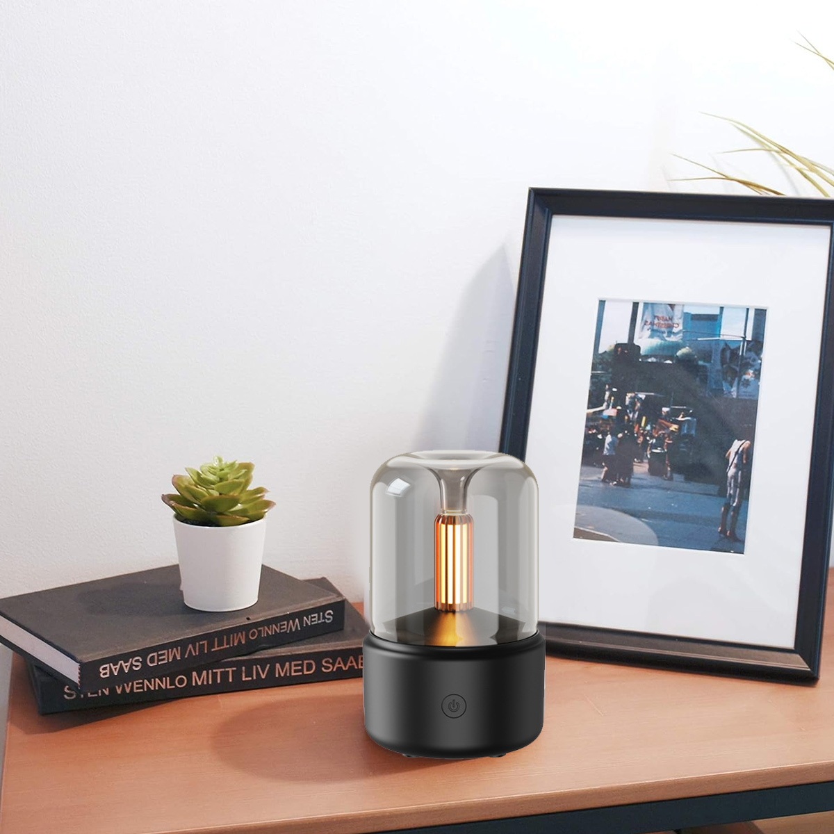 Lampe auf einem Tisch. Sie hat einen Glasschirm und einen schwarzen Sockel. Daneben stehen eine Pflanze und Bücher.