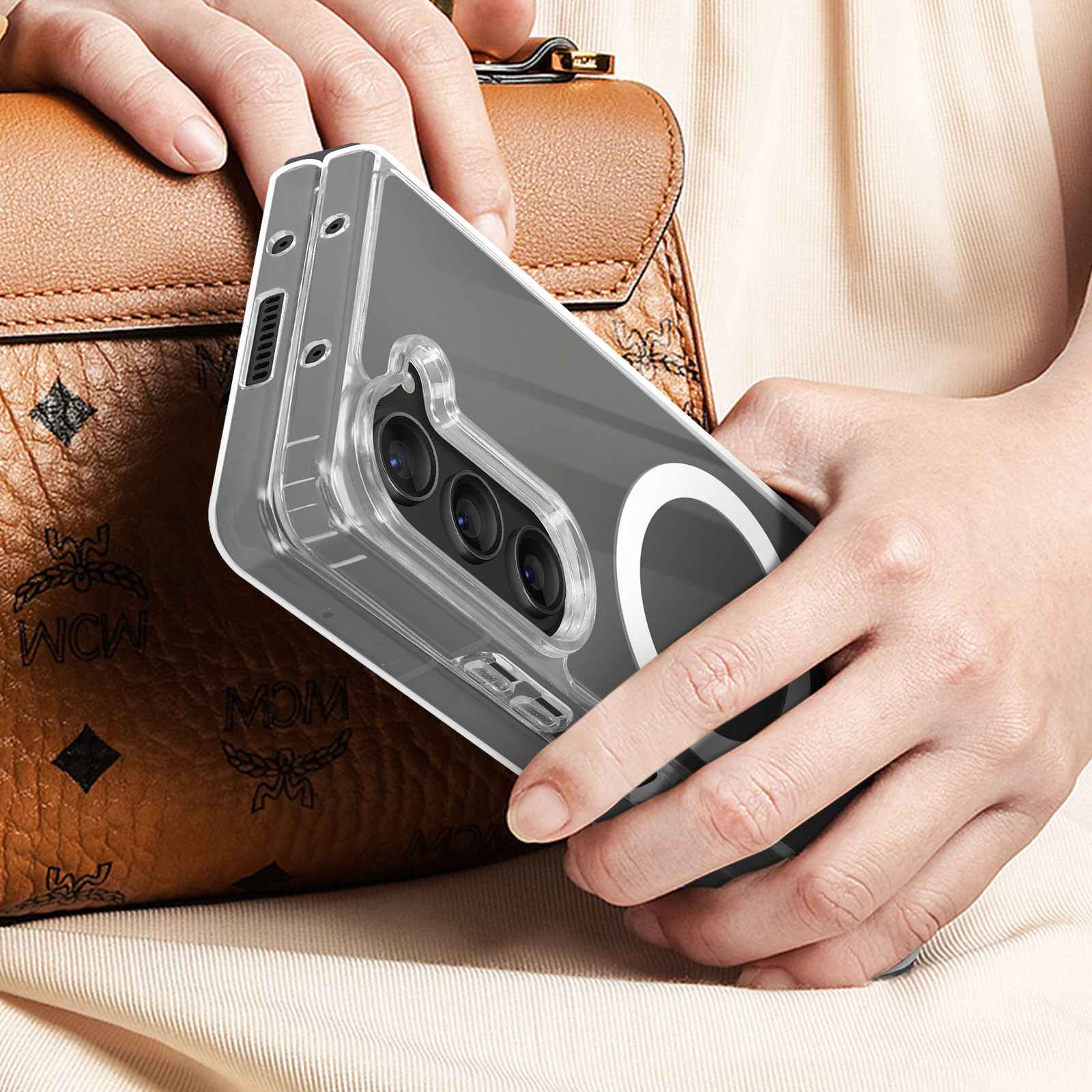 Persona che tiene in mano un telefono con una custodia trasparente. Una borsa marrone è sullo sfondo. La custodia ha un anello magnetico.
