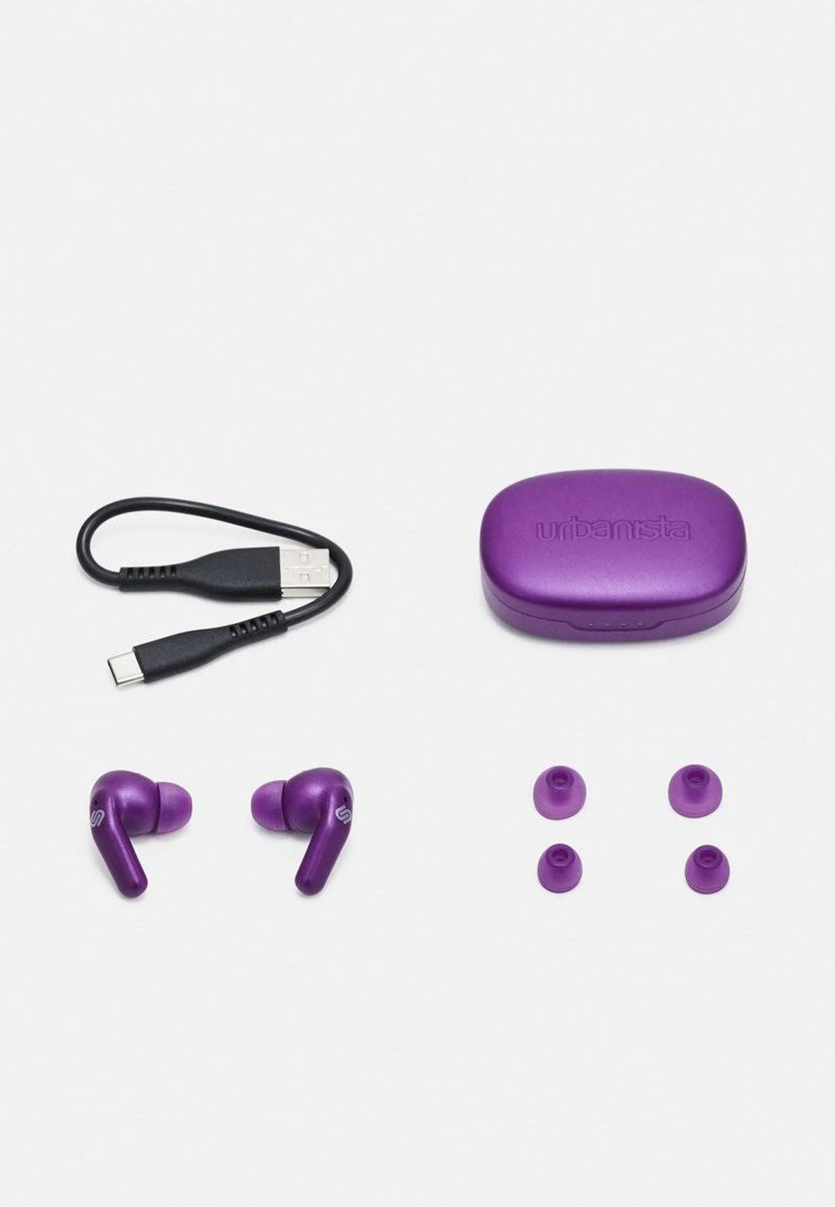Fioletowe słuchawki, etui ładujące i kabel USB na białym tle. Dodatkowe wkładki douszne są również dołączone.