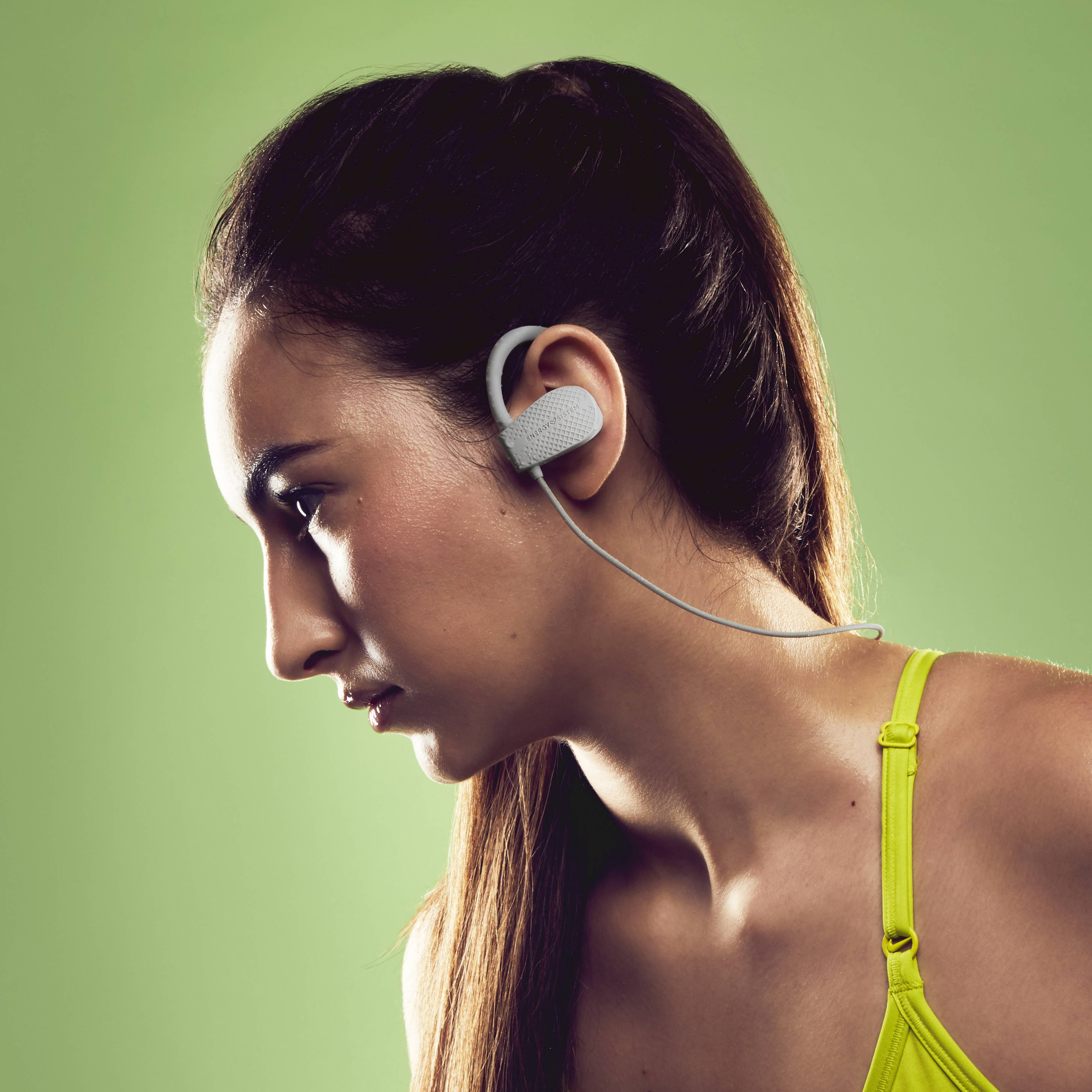 Una donna con cuffie auricolari grigie e un reggiseno sportivo giallo. Lo sfondo è verde.
