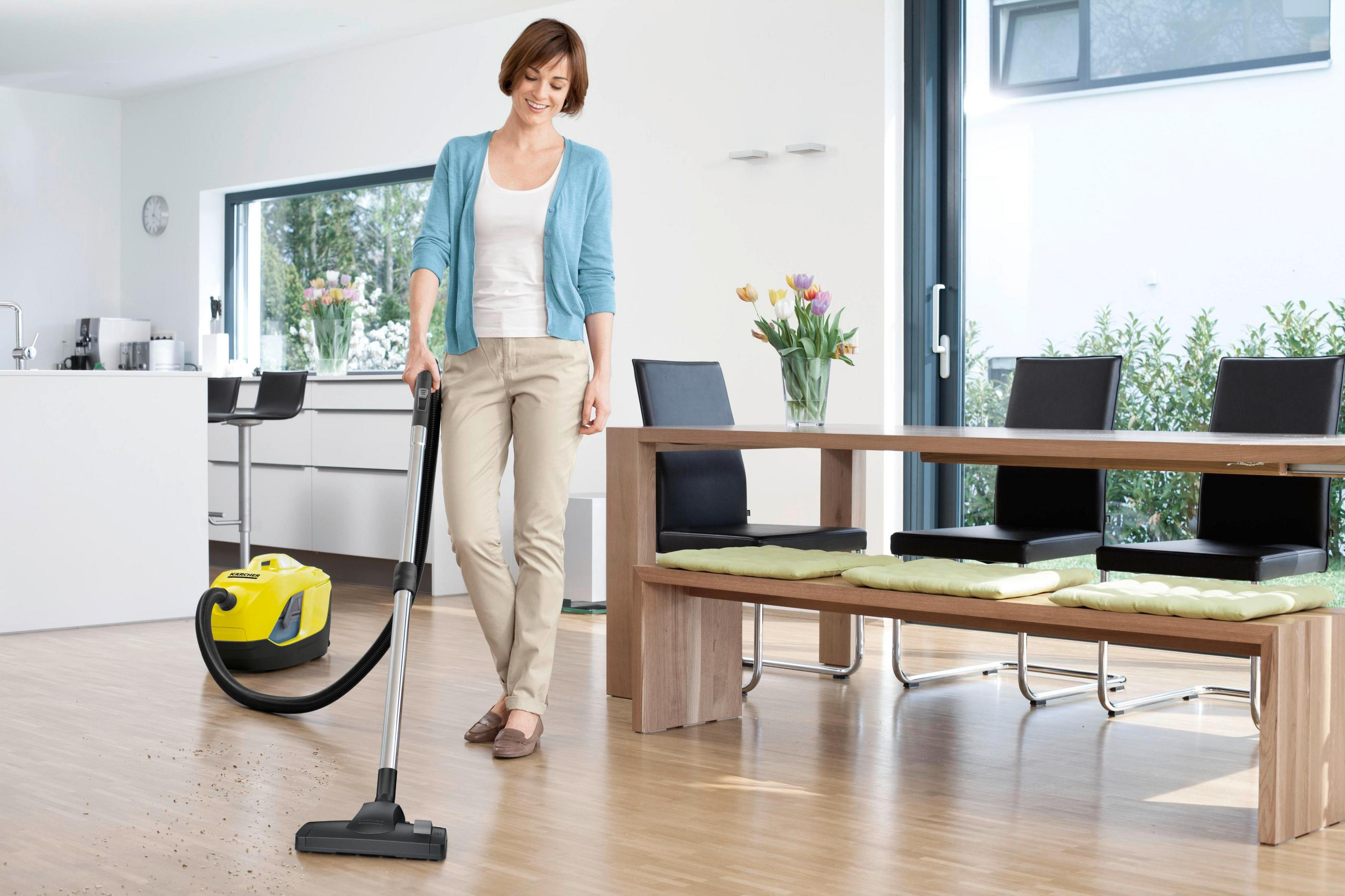 Una mujer aspira un suelo de madera en un salón moderno y luminoso.