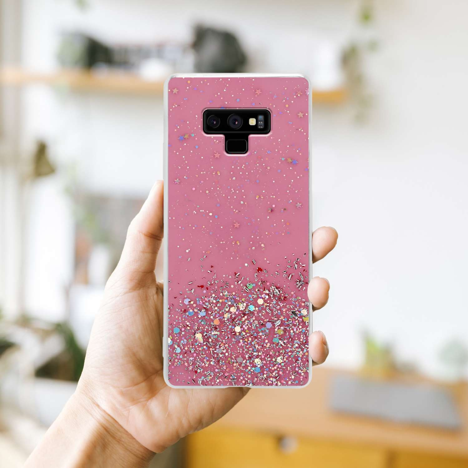 Hand hält eine pinke Handyhülle mit Glitzer. Die Hülle hat einen pinkfarbenen Farbverlauf und Glitzerdetails.