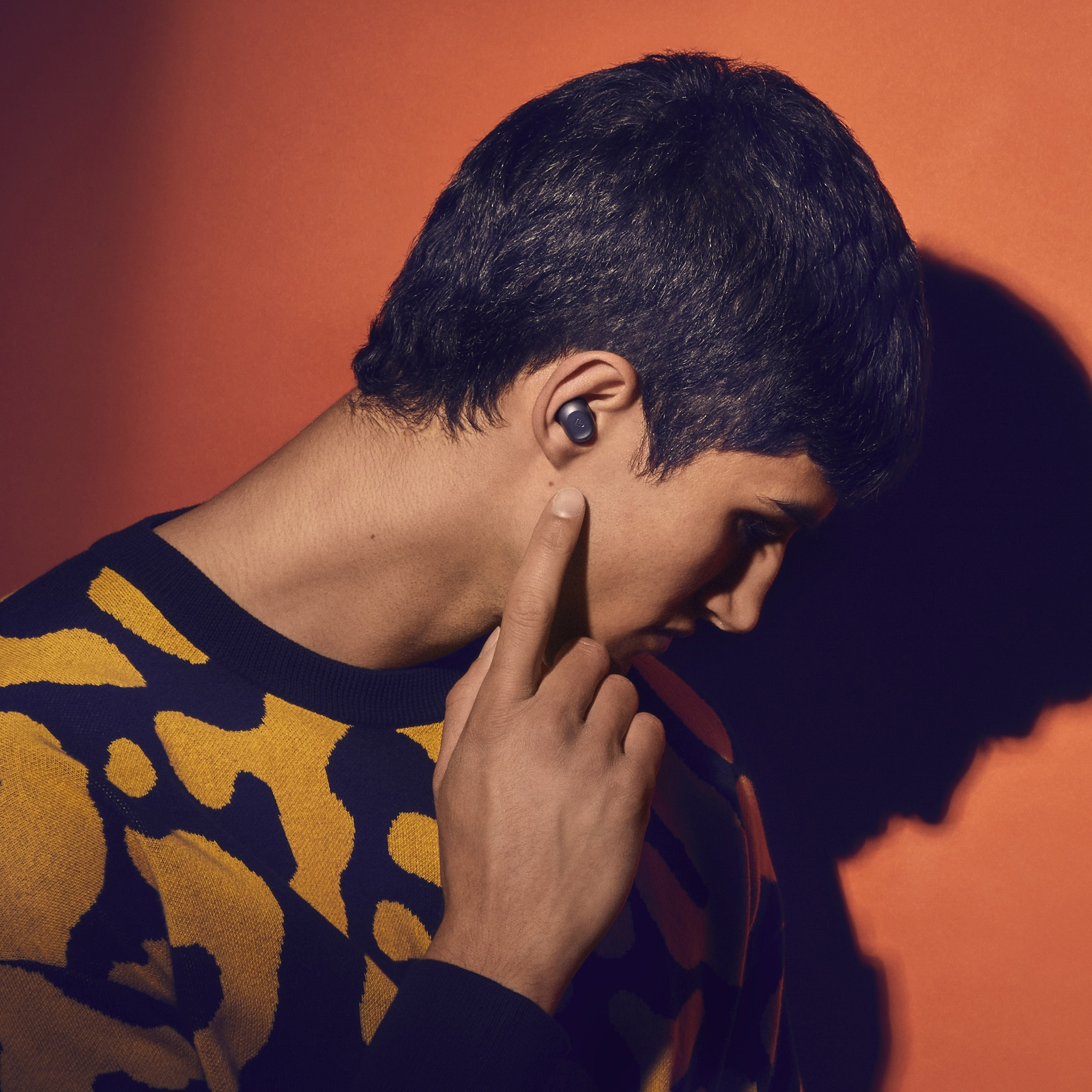 Un hombre con cabello oscuro, con un jersey amarillo y negro, tocando un auricular.