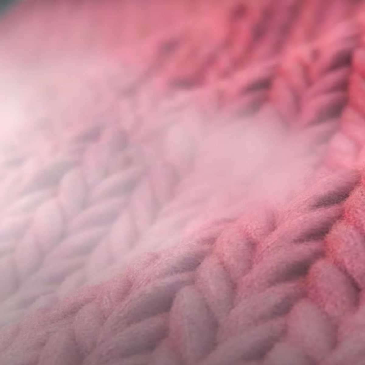 Zbliżenie na różową dzianinę. Tkanina ma miękki, teksturowany wygląd z rozmytymi krawędziami.