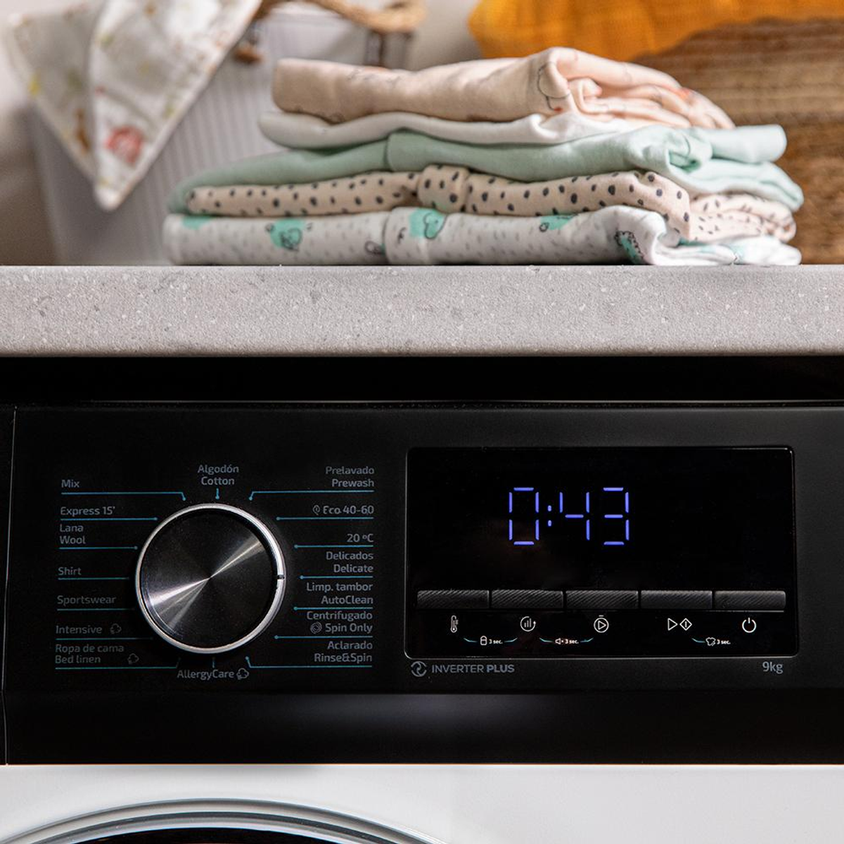 Panel sterowania pralki. Stos złożonych ubranek dziecięcych na górze maszyny.