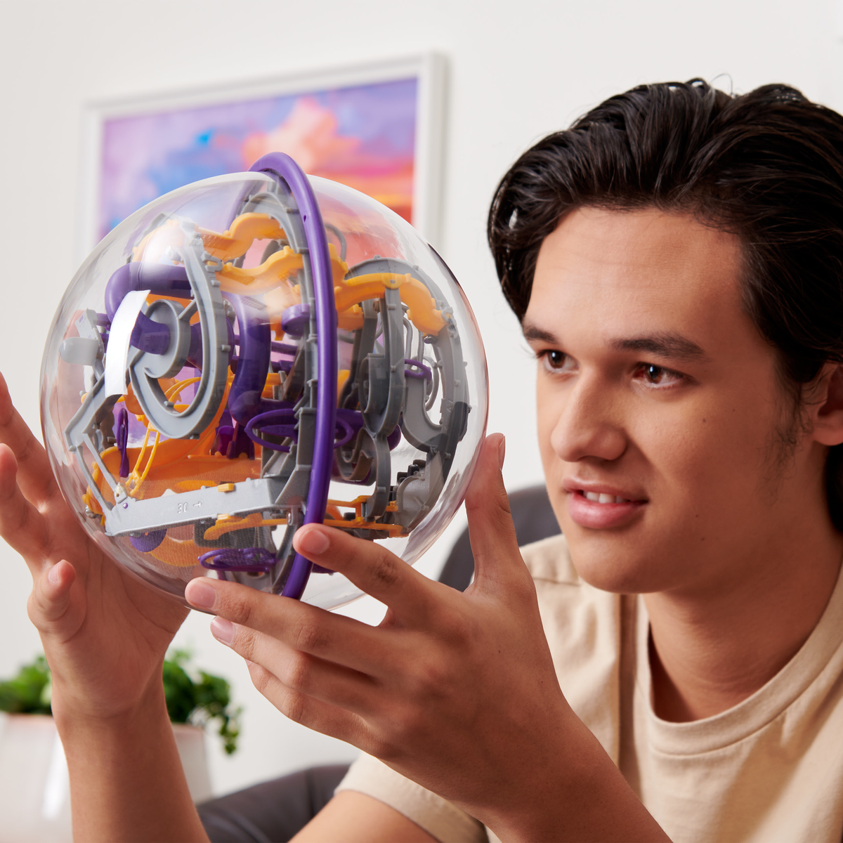 Un giovane uomo che tiene una palla puzzle trasparente con un labirinto complesso all'interno, sfondo sfocato.