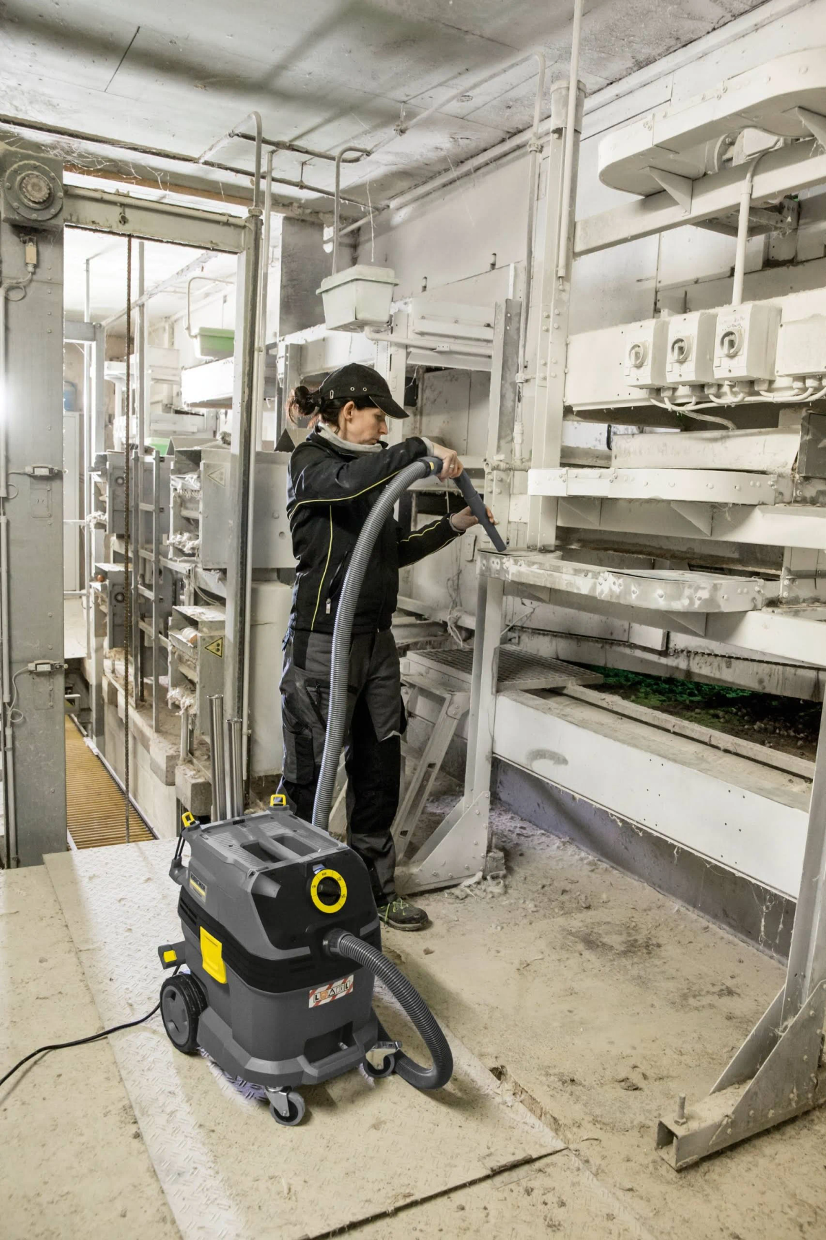 Kobieta w fabryce sprząta odkurzaczem, w białym środowisku przemysłowym.