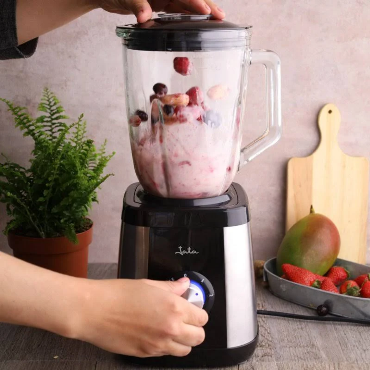 Una licuadora en uso, agregando ingredientes al vaso de la licuadora.
