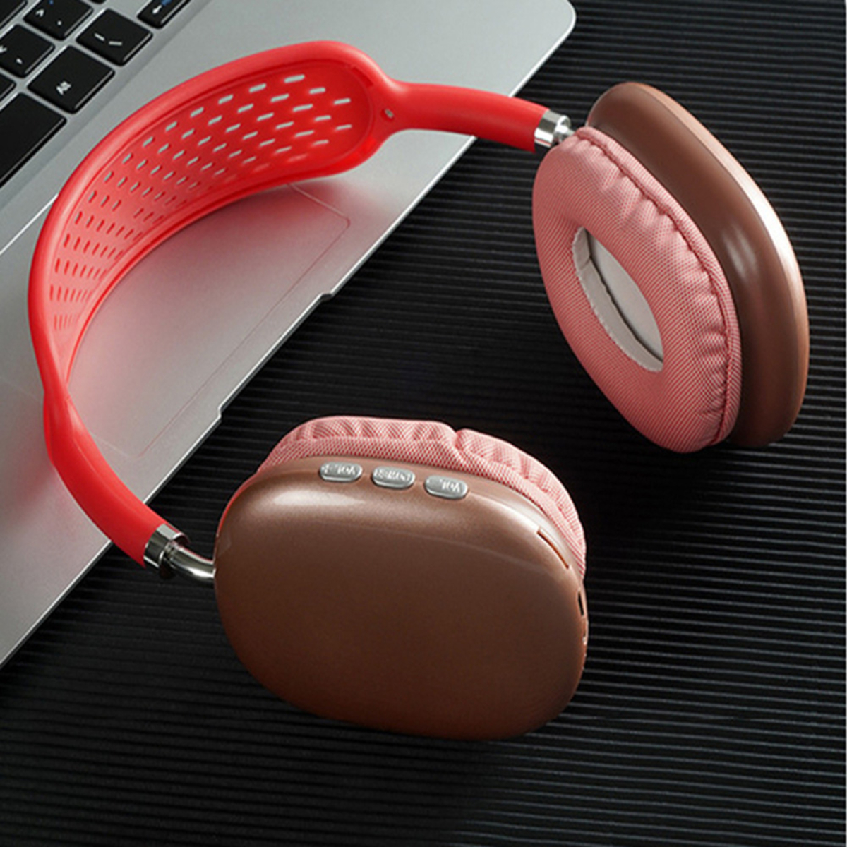 Auriculares rojos y marrones sobre un portátil. Los auriculares tienen una banda roja y almohadillas marrones. El fondo es oscuro.